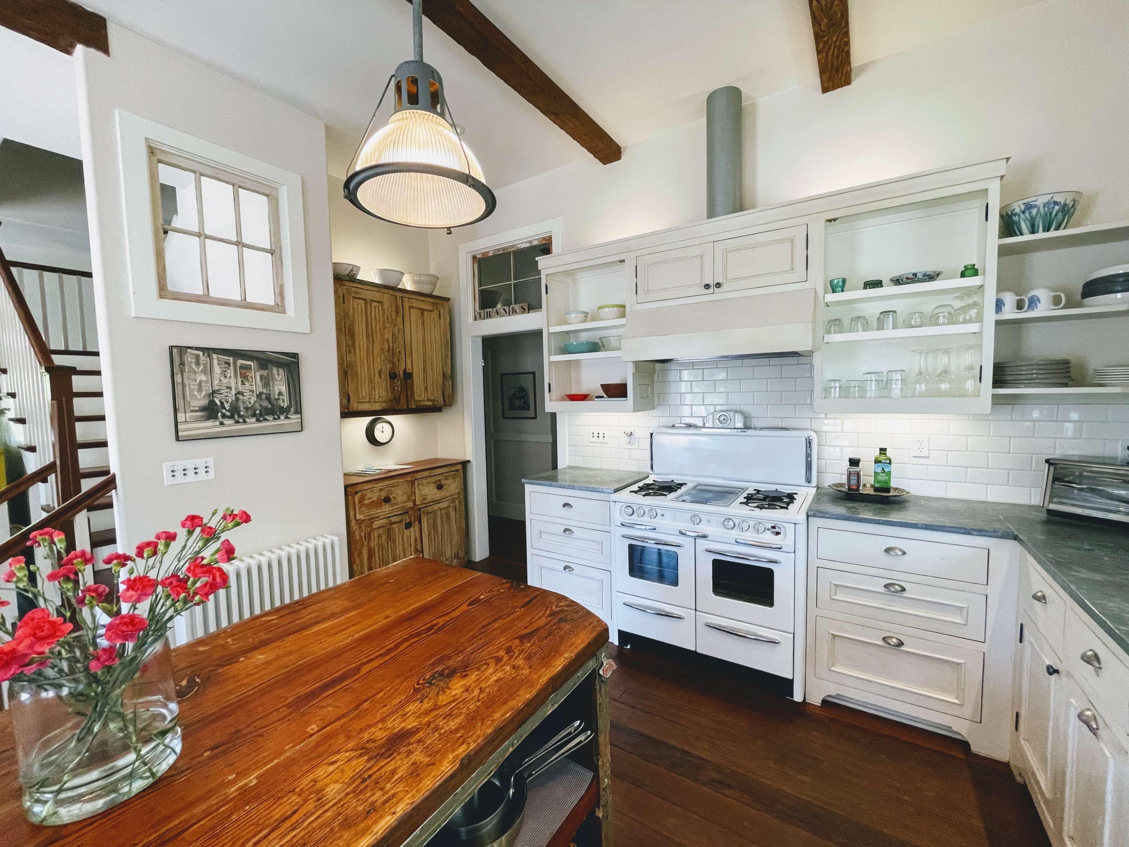 A modern kitchen with white cabinetry, a vintage stove, wooden accents, and a central island with a vase of flowers.