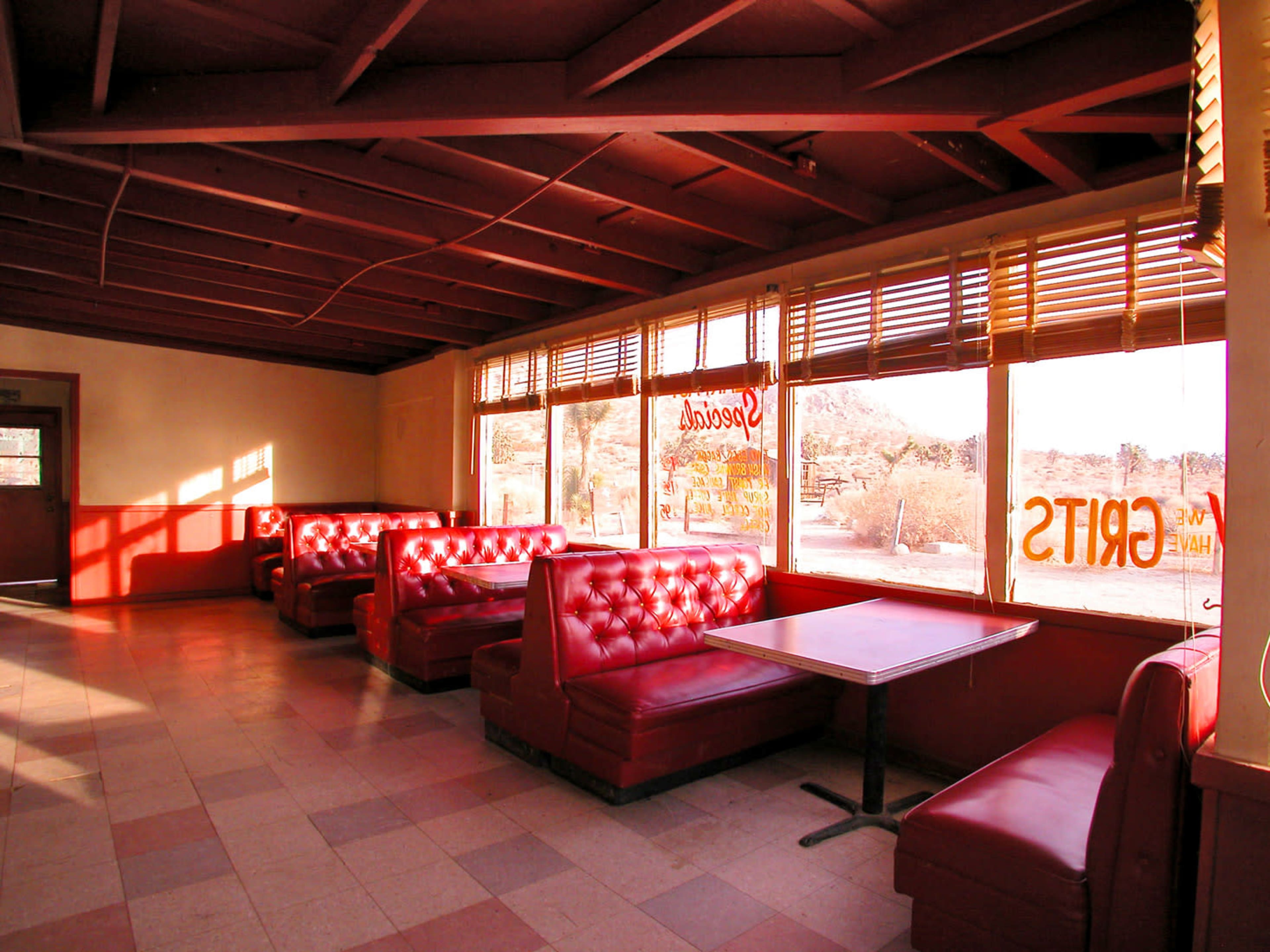 The image shows a retro diner interior with red leather booths and large windows allowing natural light to enter.