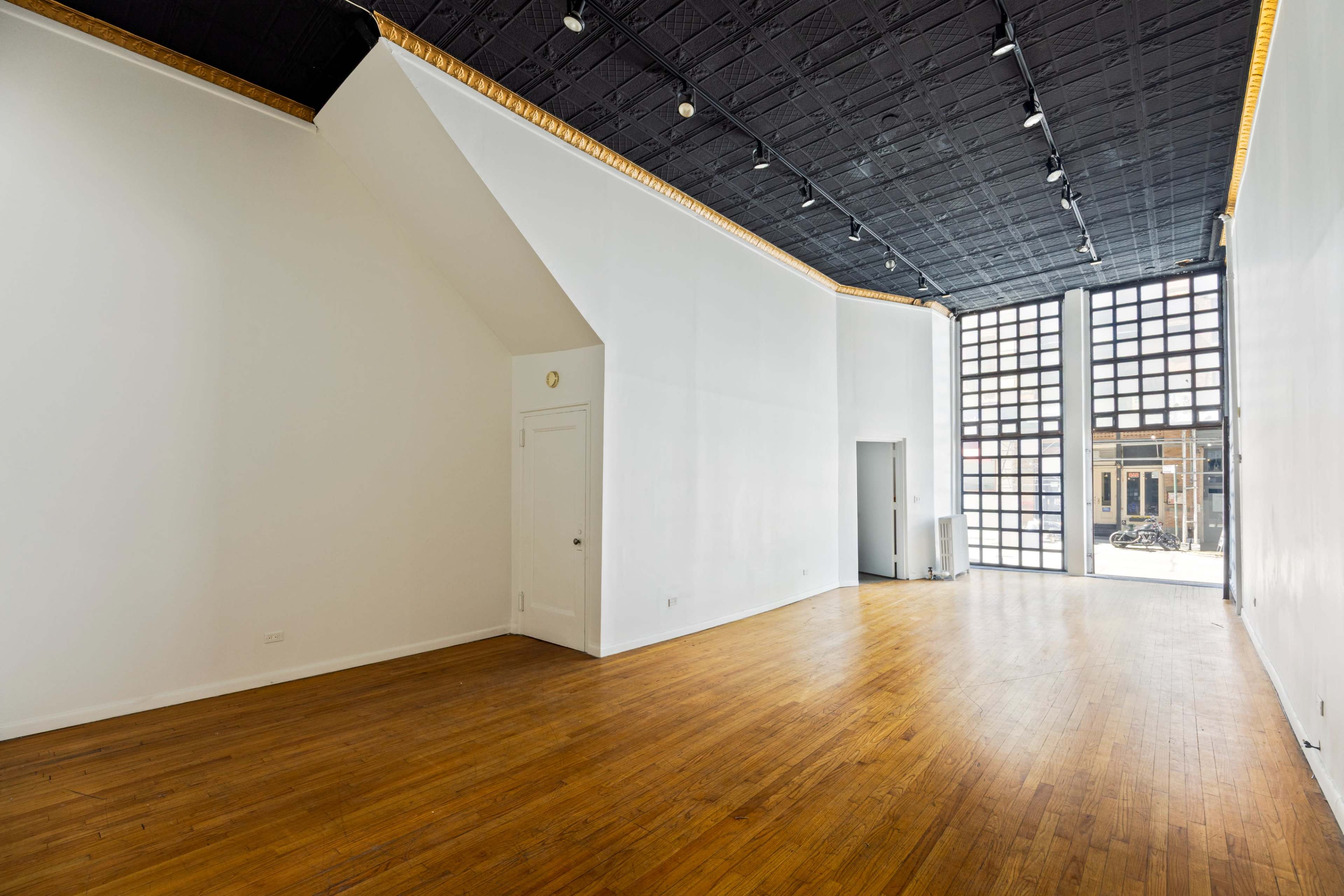 The image shows an empty, well-lit commercial space with hardwood flooring and large windows.