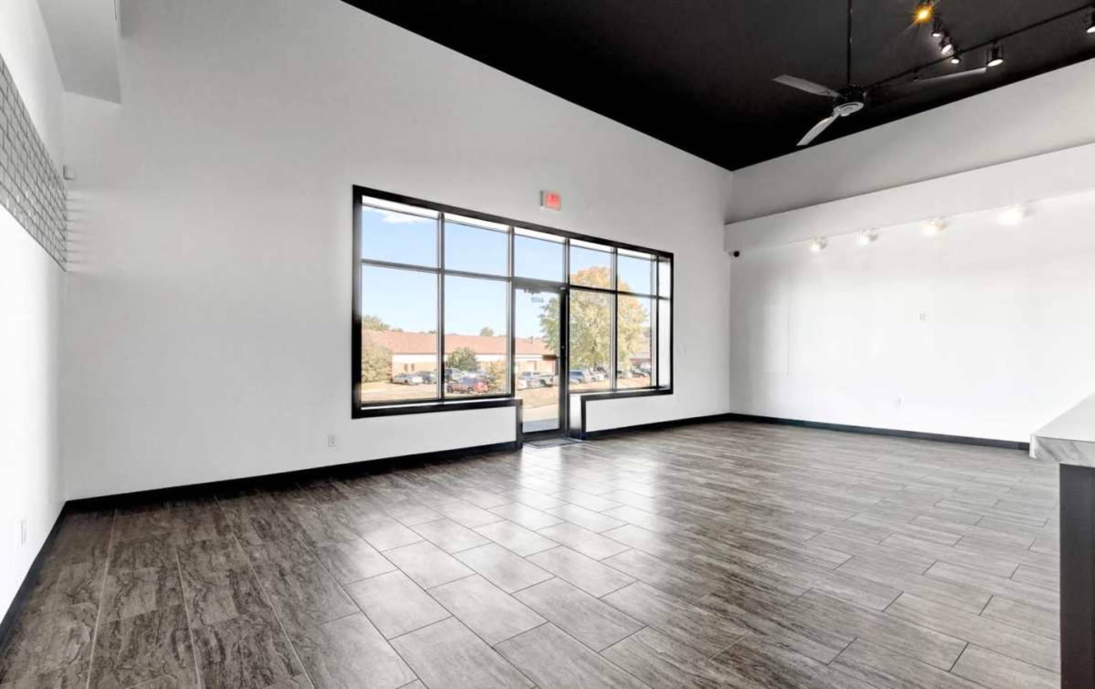 The image shows a spacious, empty room with large windows and dark tiled flooring.