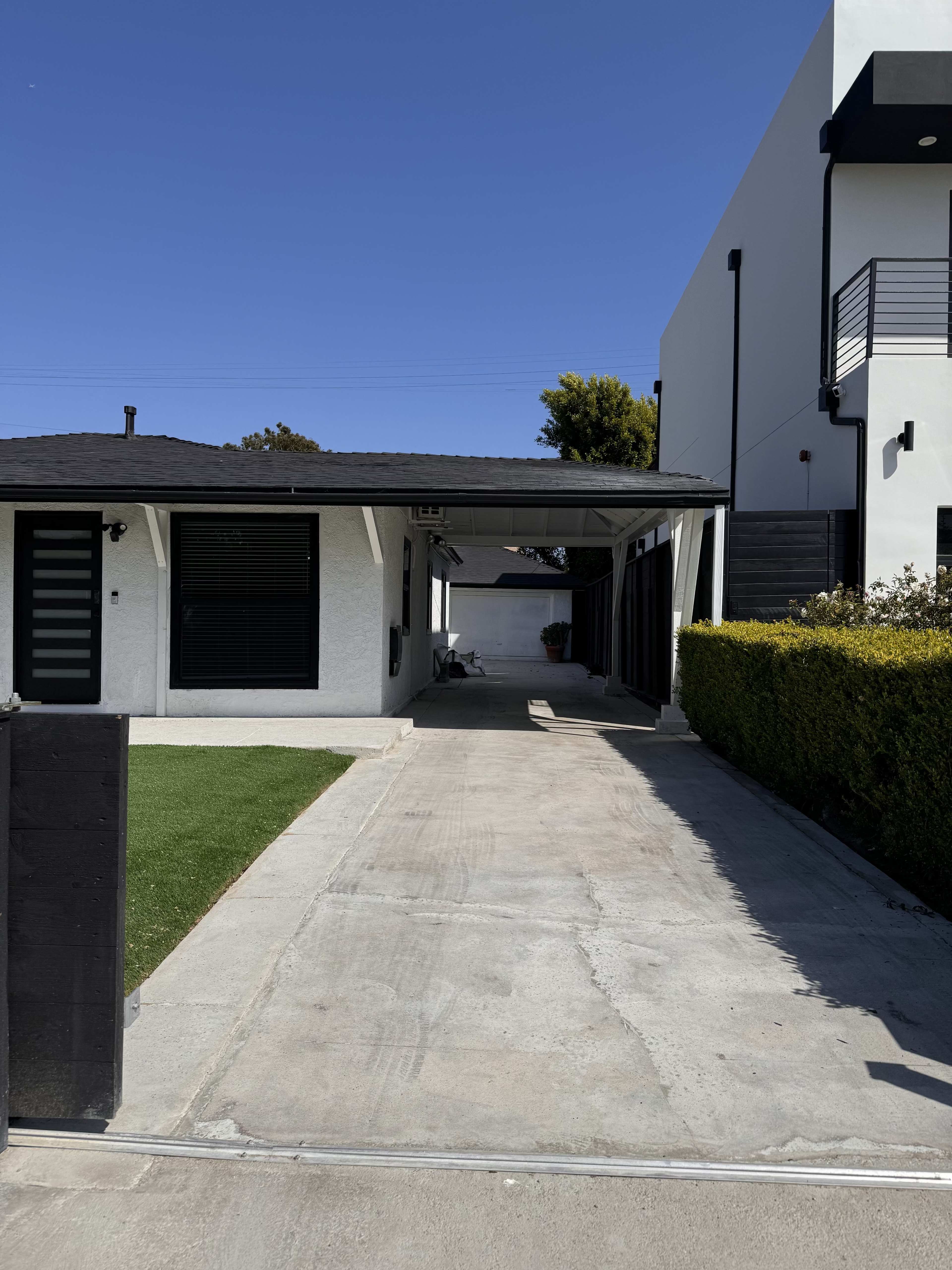 The image shows a driveway leading to a garage beside a white house with a black roof and clean landscaping.