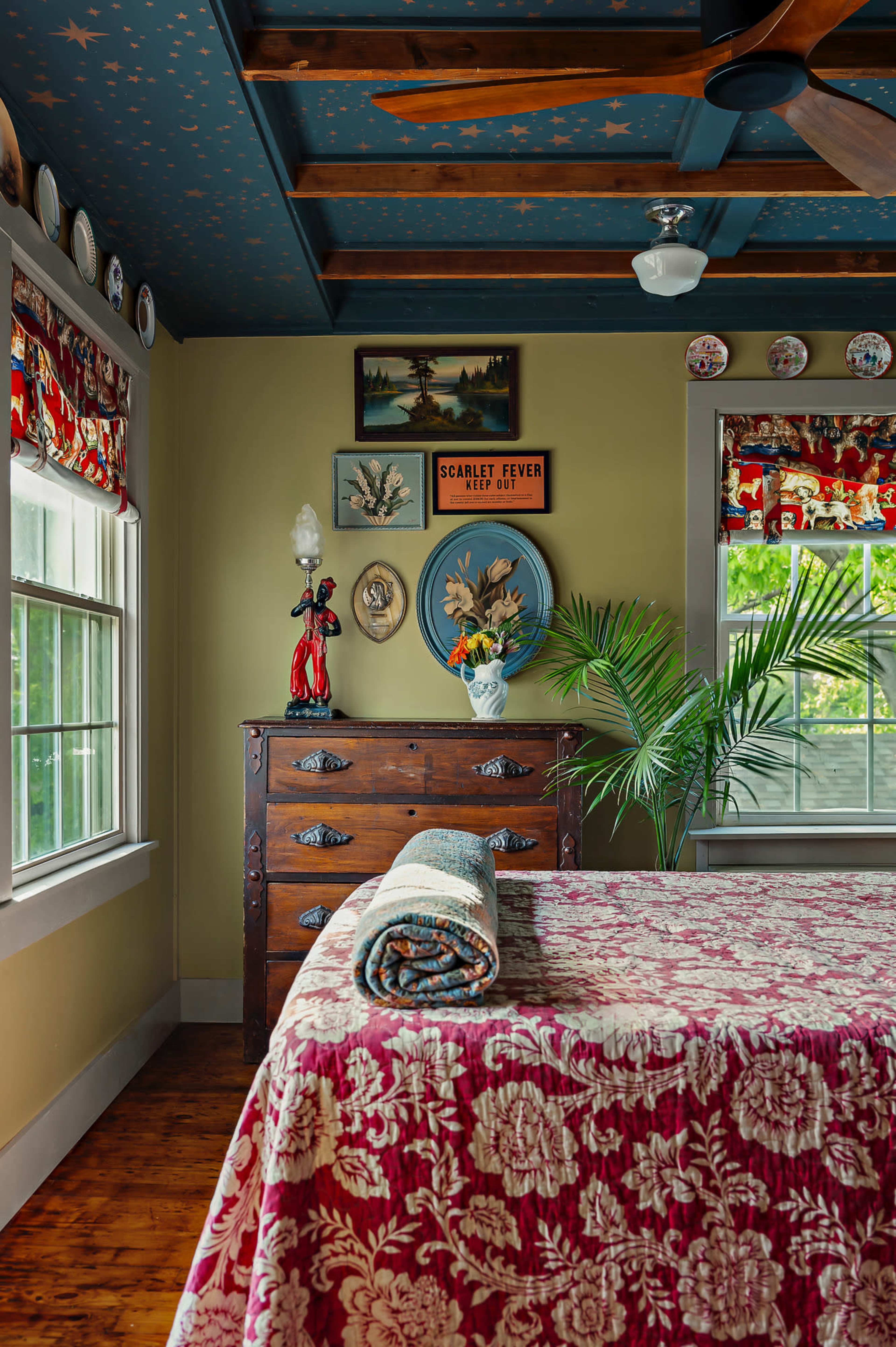 A neatly arranged bedroom features a large bed with a patterned quilt, a wooden dresser adorned with decorative items, and starry blue ceiling above.