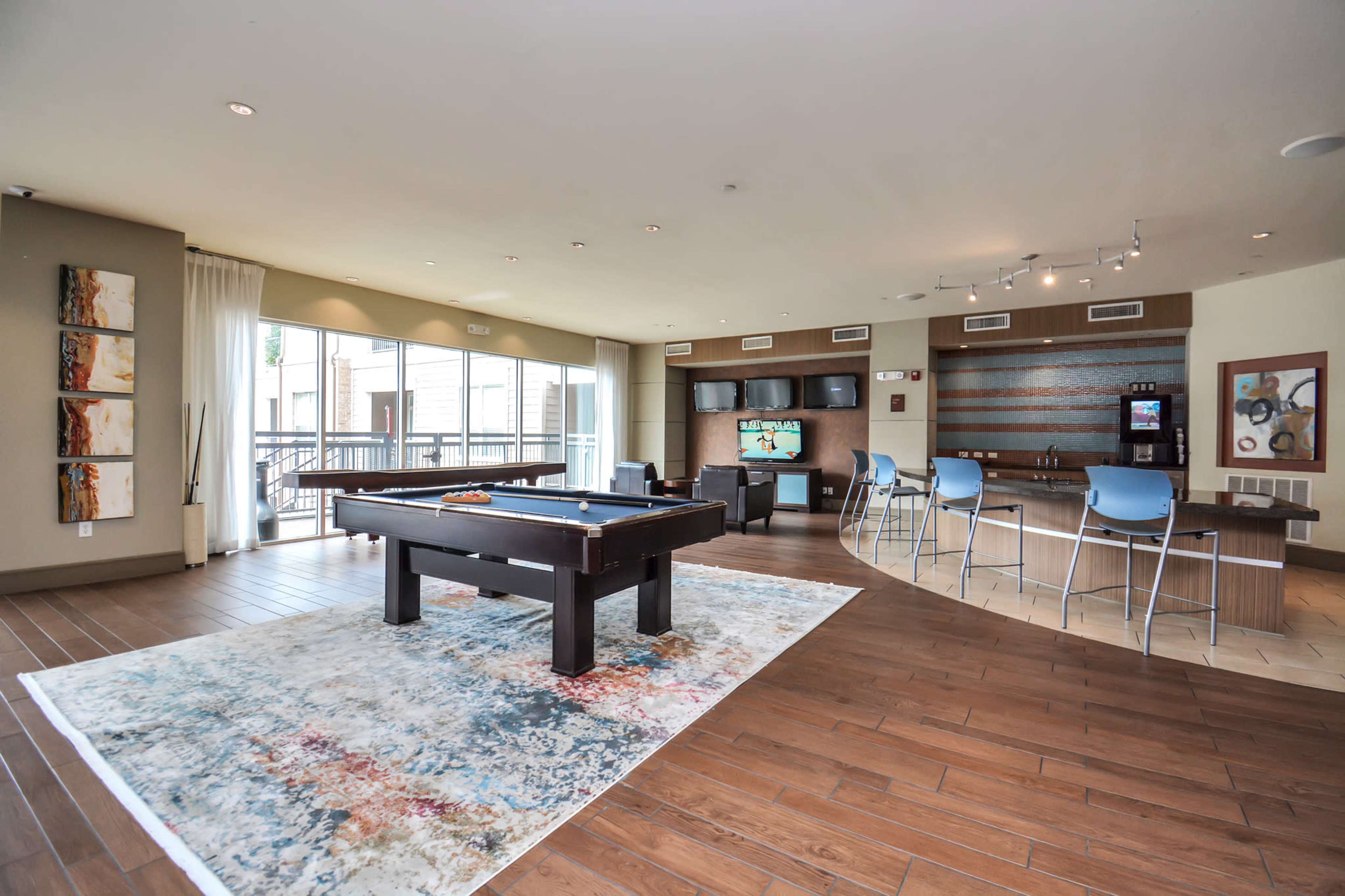 A spacious recreation area featuring a pool table, seating, and a bar along with large windows allowing natural light.