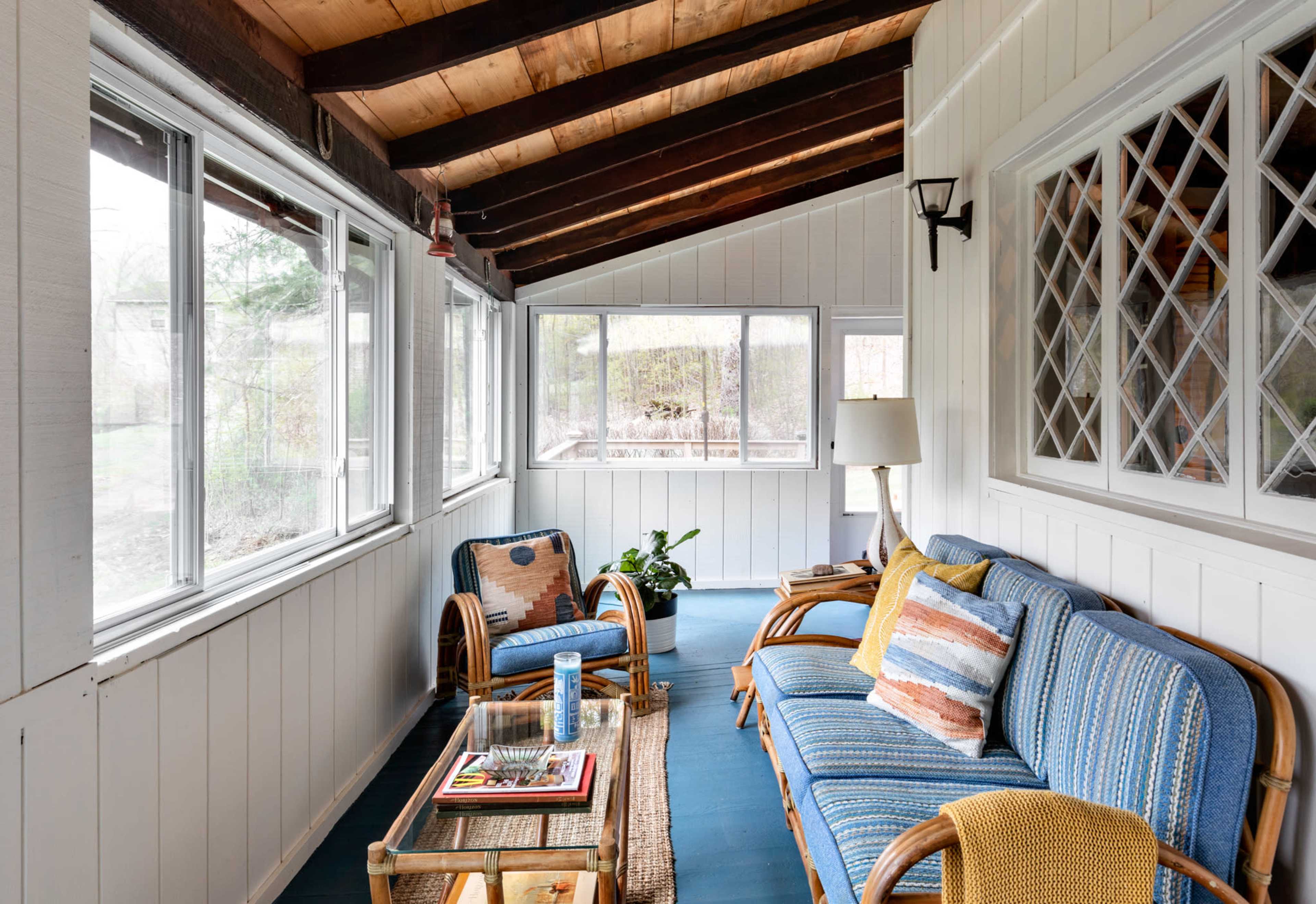 A sunroom featuring a blue couch, wicker chairs, and large windows that provide natural light.
