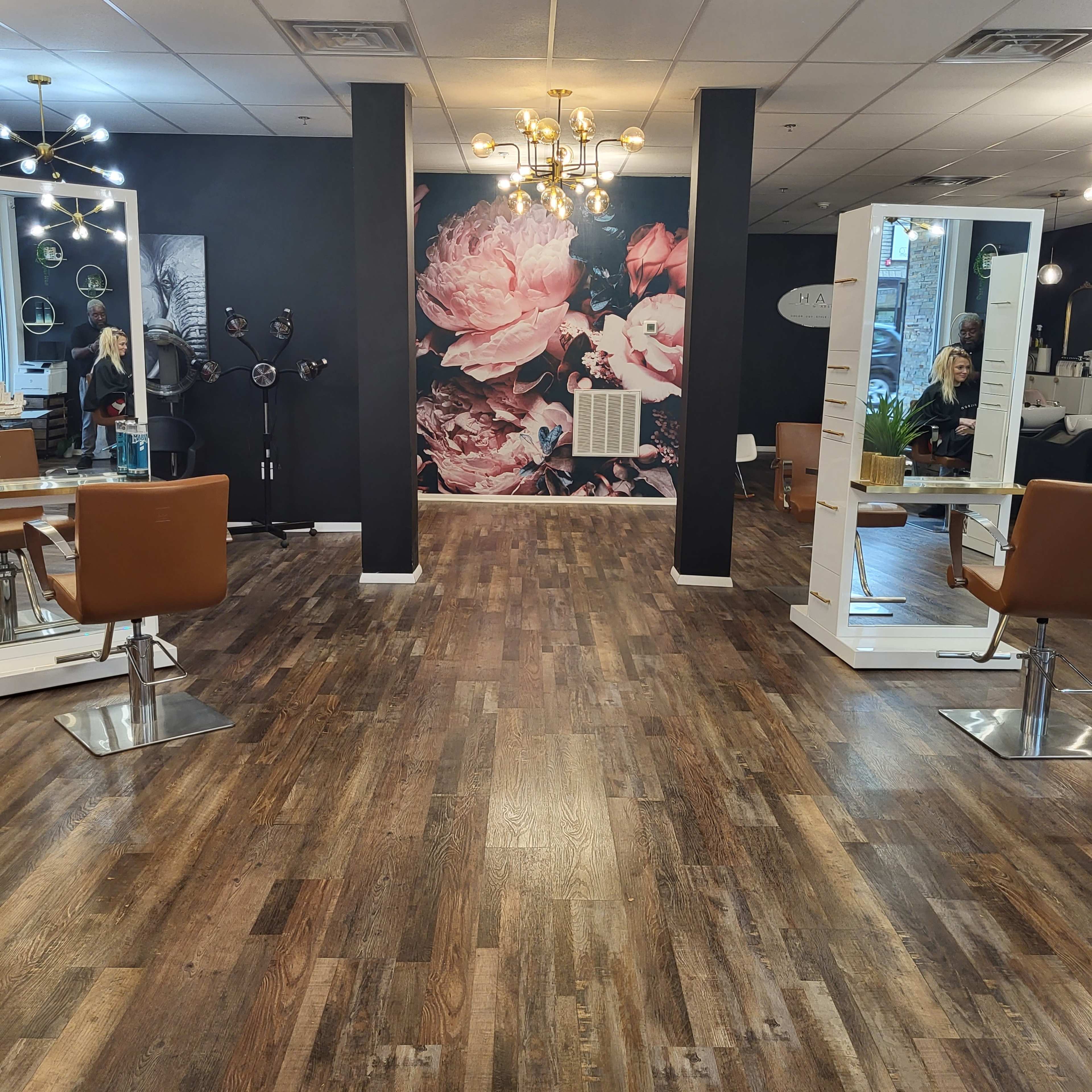 A modern hair salon featuring wooden floors, two styling stations with mirrors, and a large floral mural on the back wall.