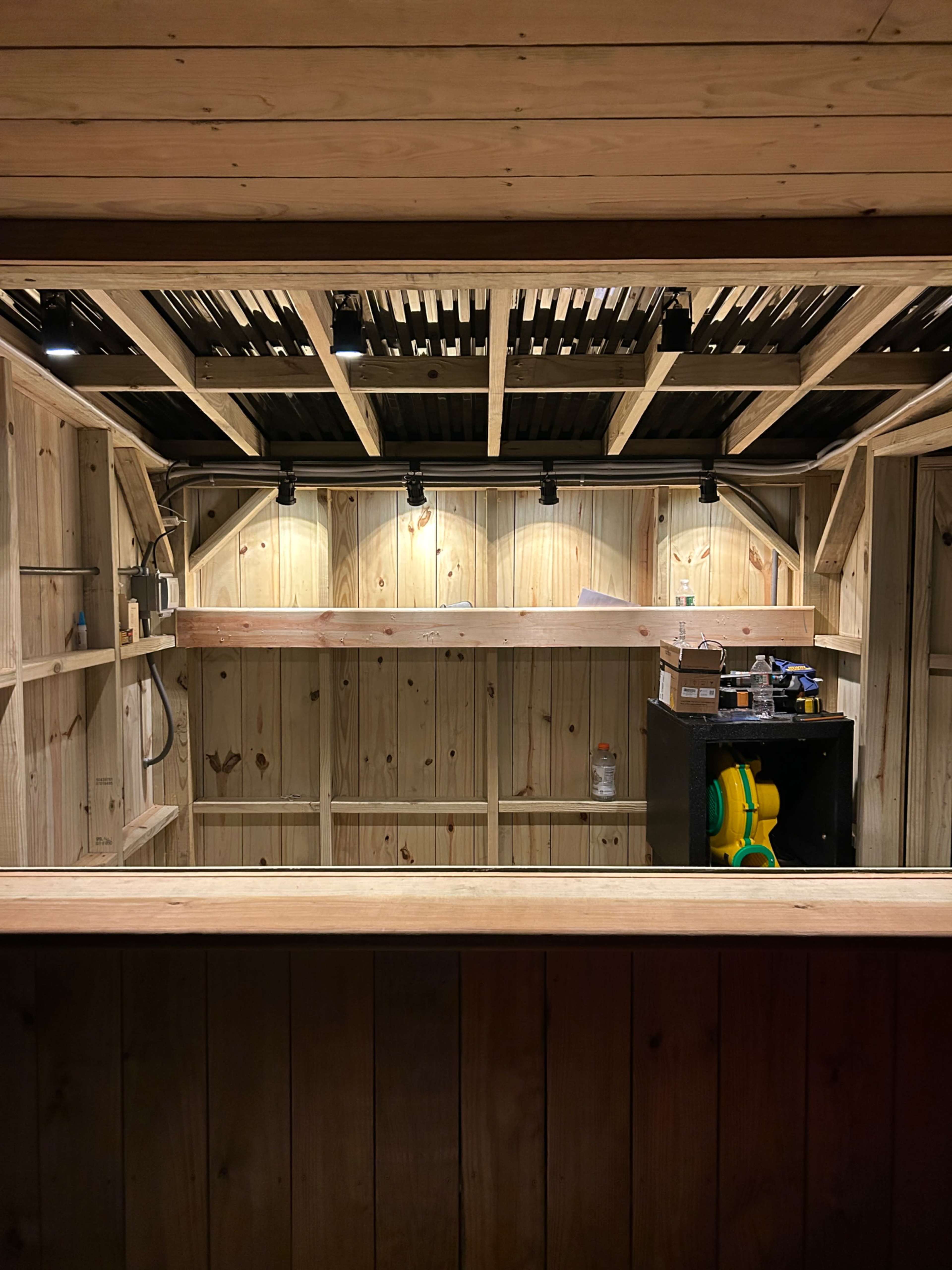 The image shows an unfinished wooden bar or counter area with shelves and lighting installed against a wall.