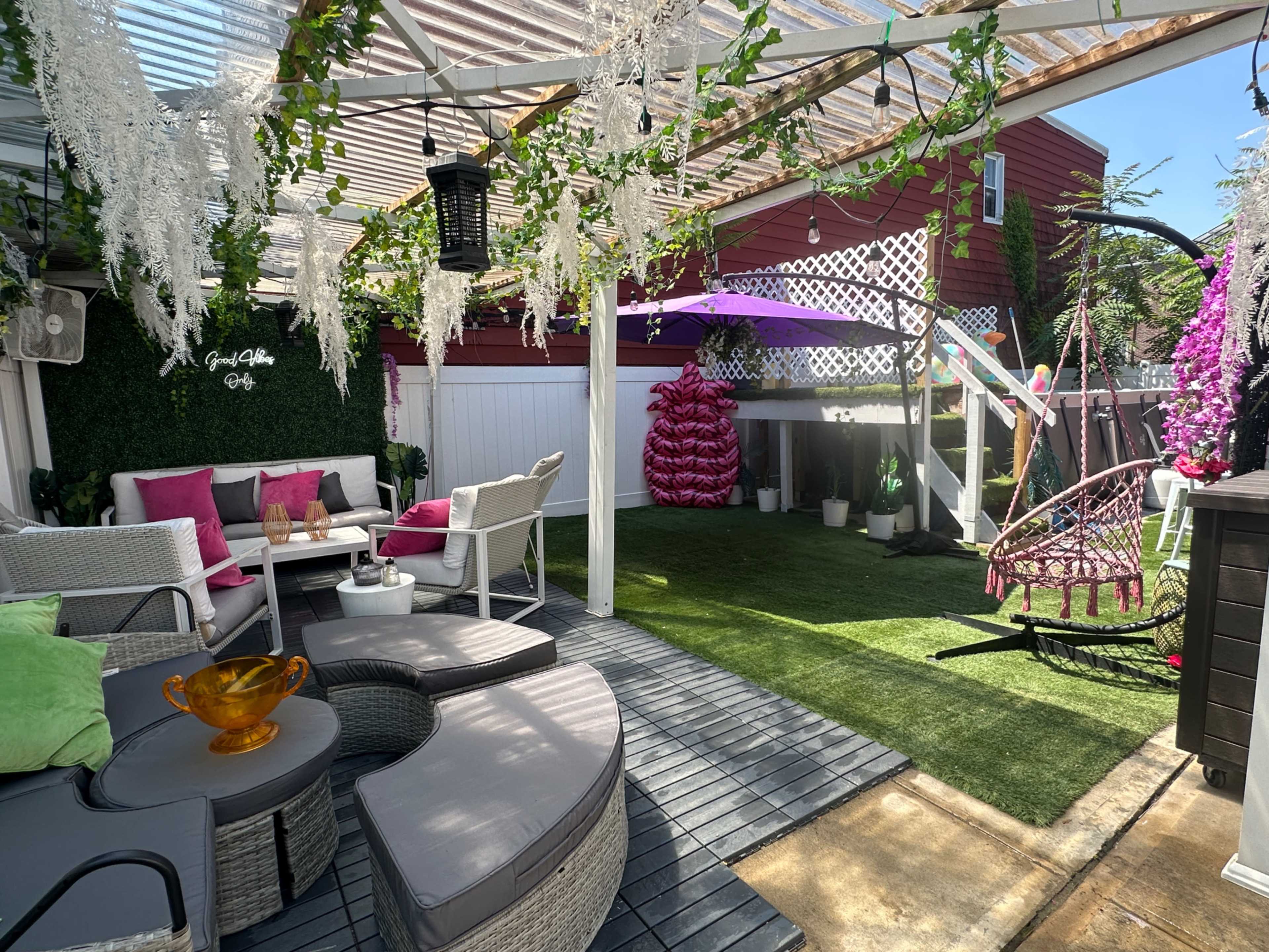 A landscaped backyard patio with seating arrangements, a swing chair, decorative plants, and a shaded area covered by a pergola.