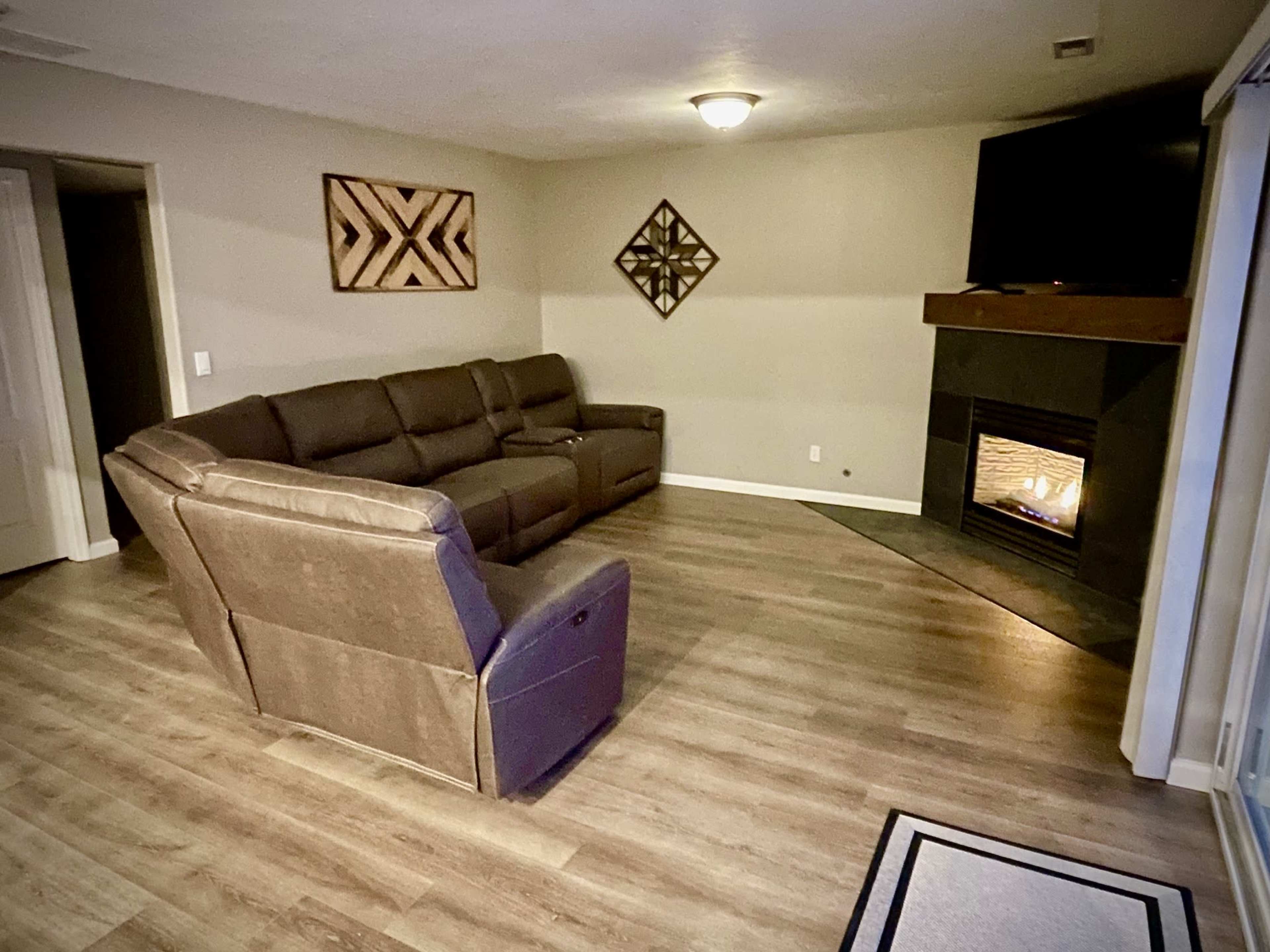 A cozy living room featuring a sectional couch, a fireplace with a TV above it, and decorative wall art.