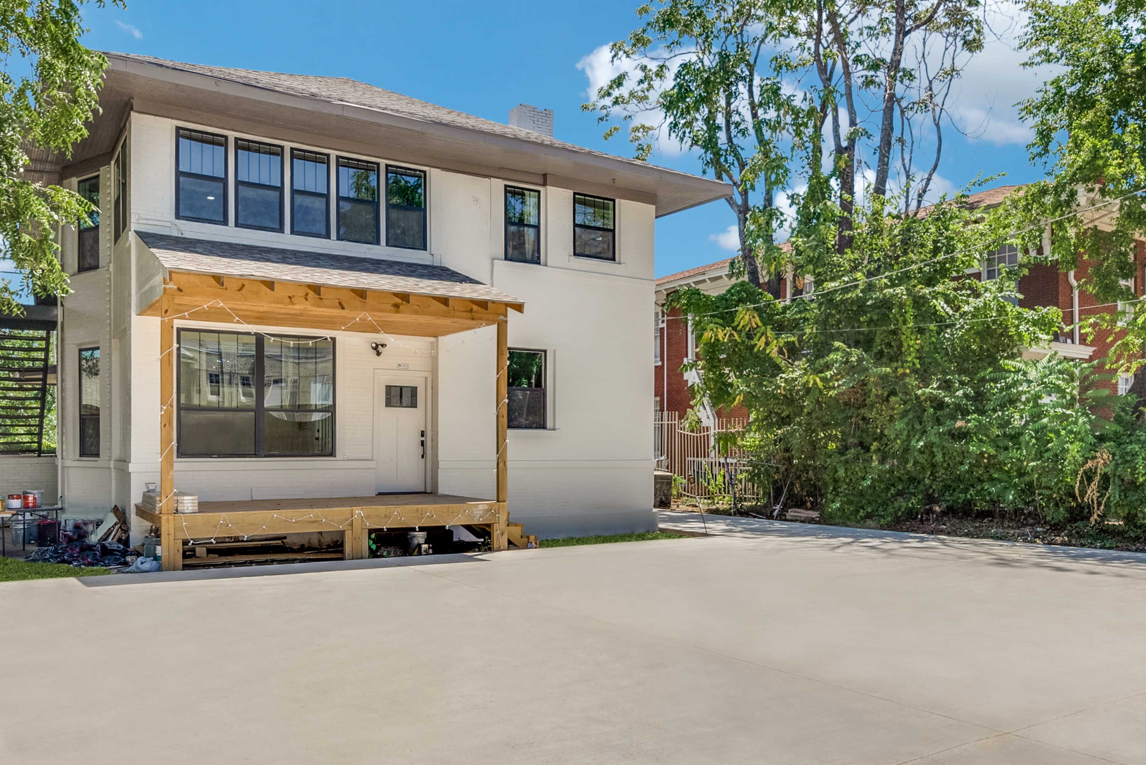 A two-story house with a covered front porch is surrounded by trees and green space.