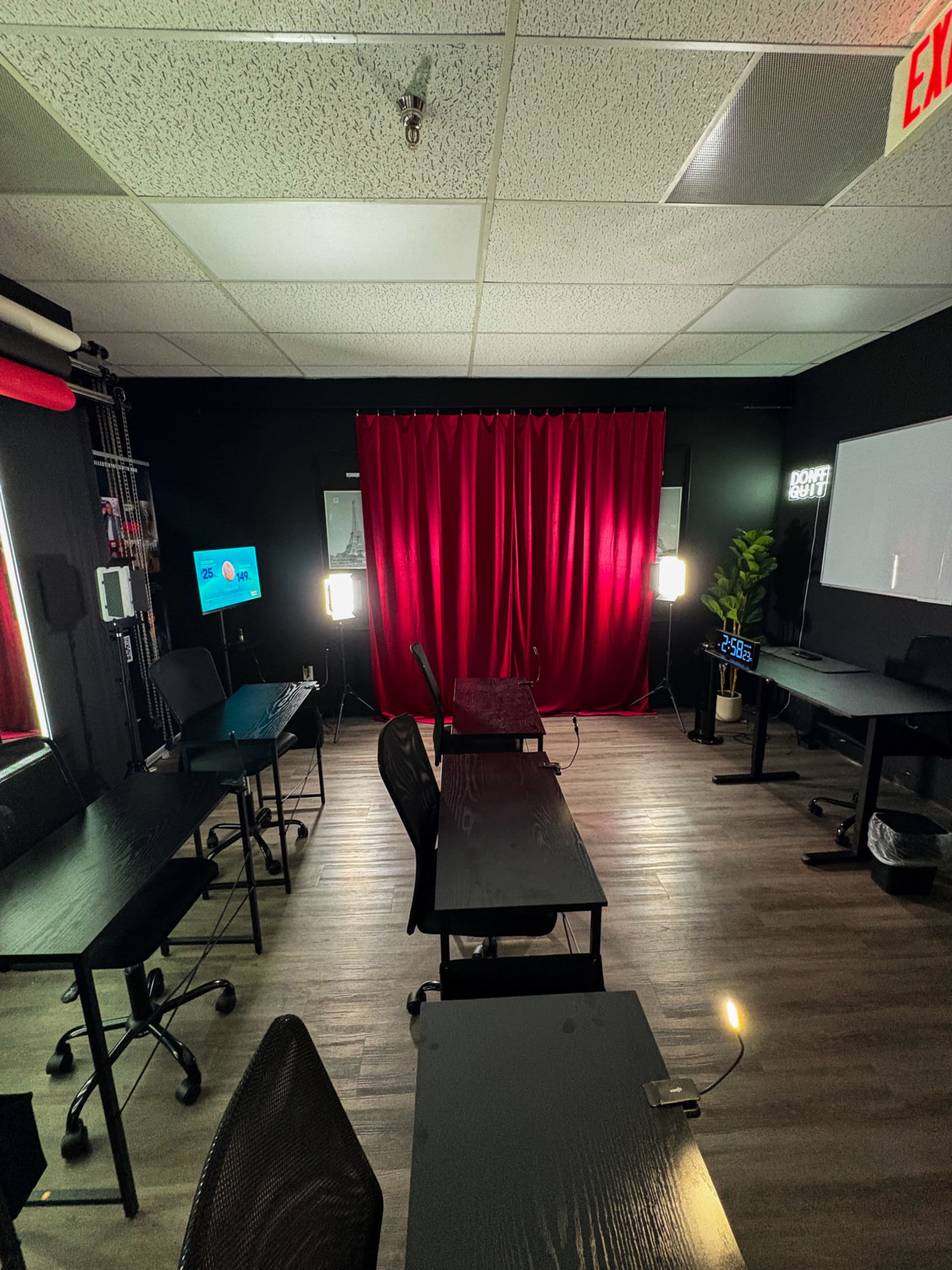 The image shows a dimly lit room with several desks arranged in a row, a red curtain at one end, and two artificial lights positioned to illuminate the space.