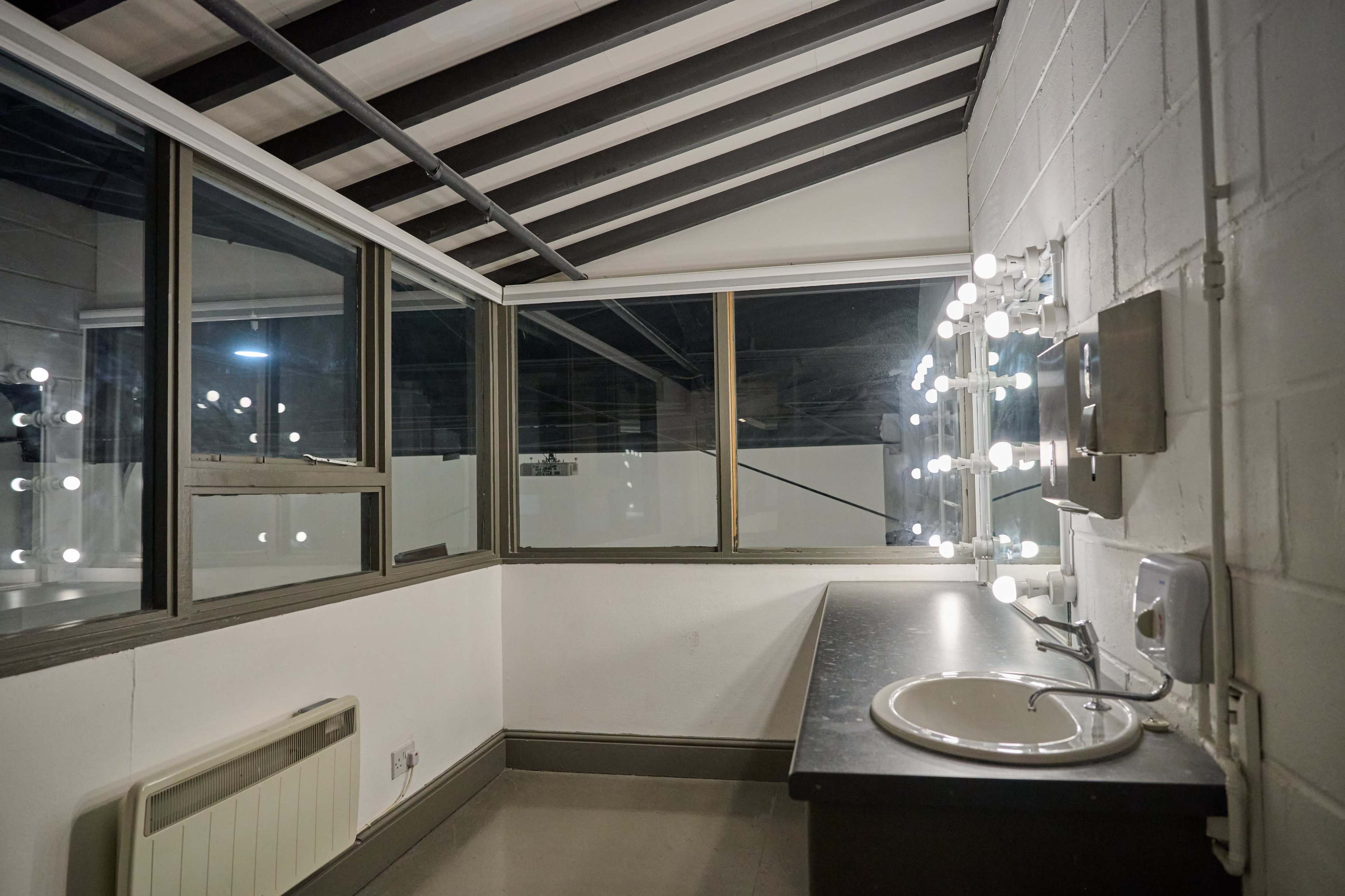 The image shows a brightly lit dressing room with a mirror and vanity area, featuring a sink and large windows.
