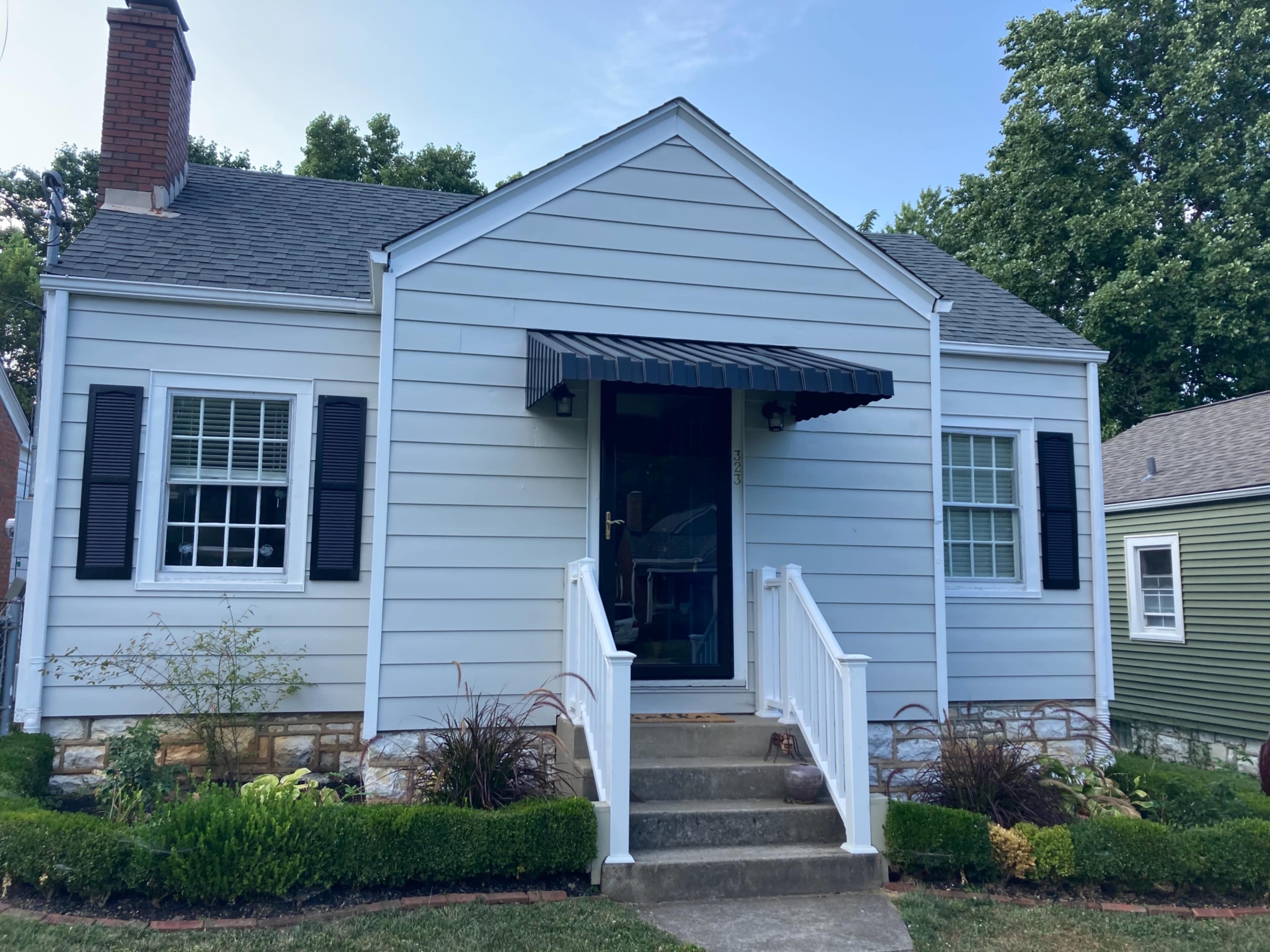 A blue, single-story house with a front porch, white railings, and black shutters.