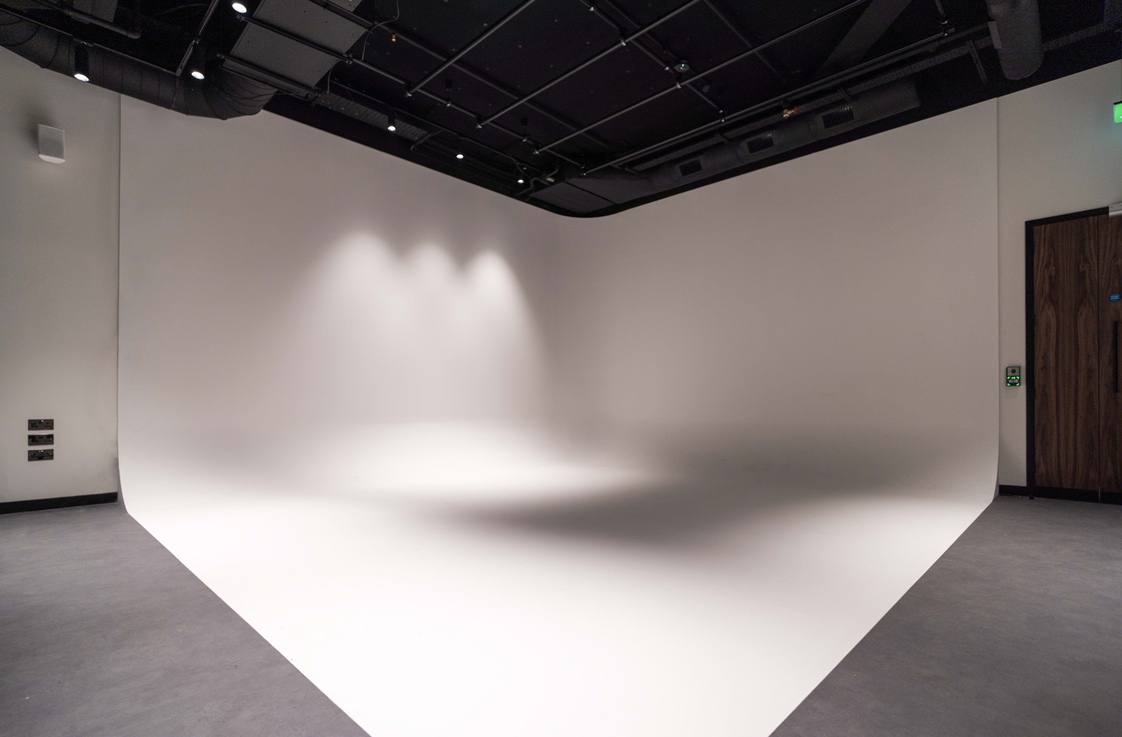 The image shows a spacious studio with a seamless white backdrop and soft lighting.