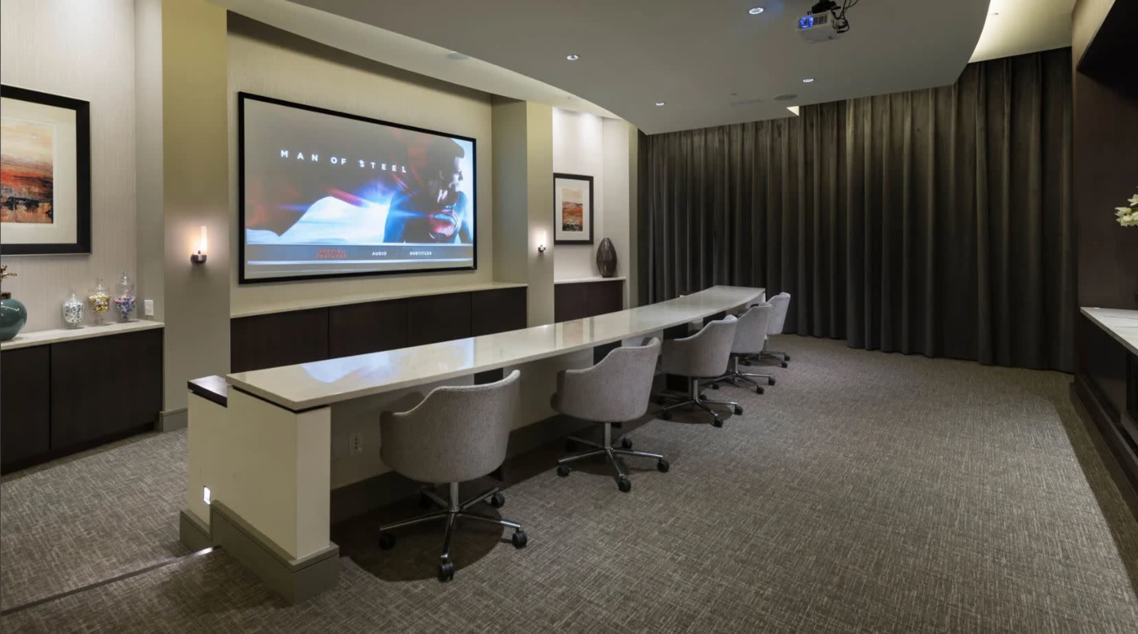 A conference room with a large screen displaying a scene from "Man of Steel" and a long table surrounded by rolling chairs.