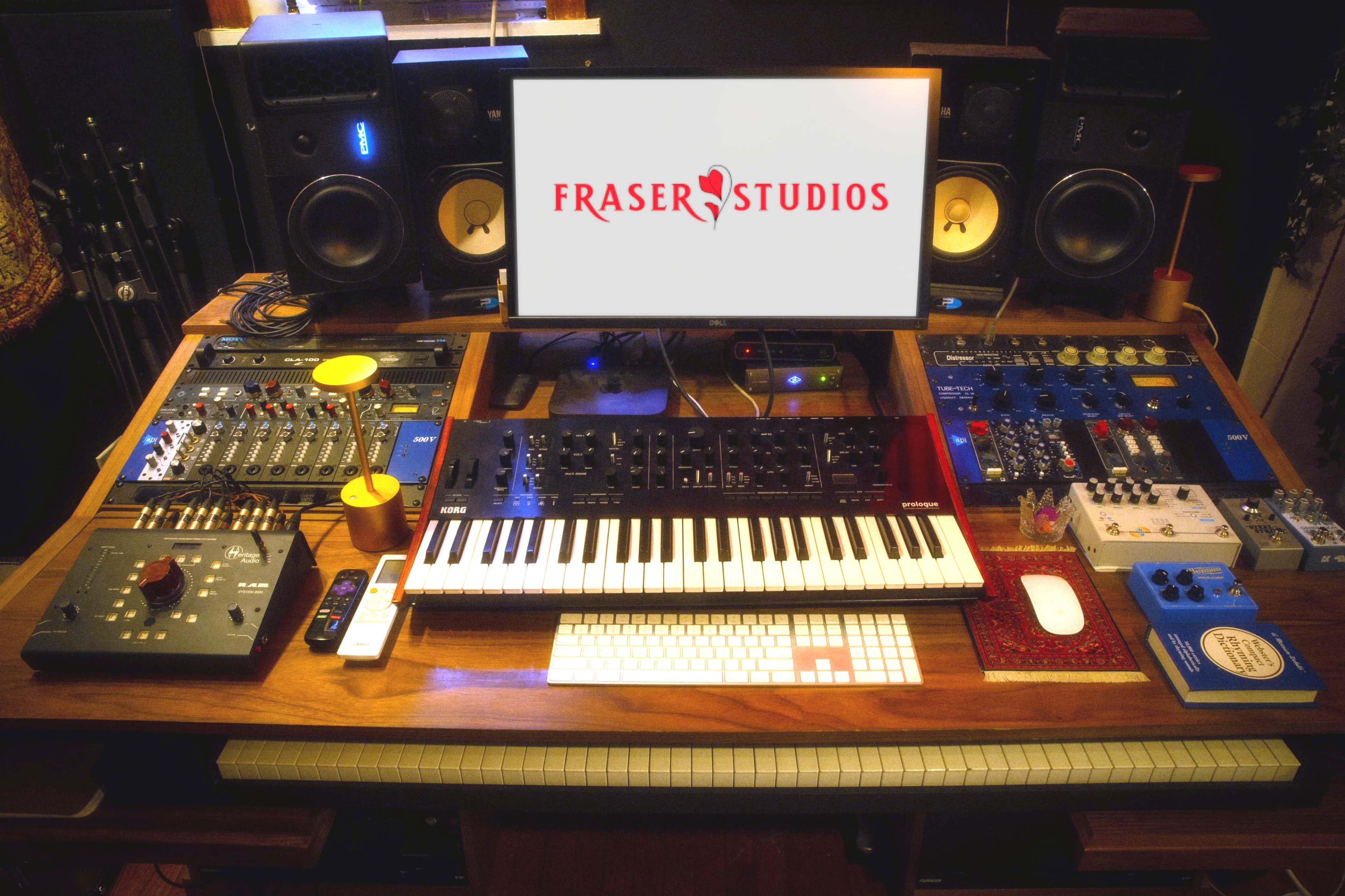 A modern music production studio setup features a central keyboard, mixing equipment, and a computer display with the logo "FRASER STUDIOS."