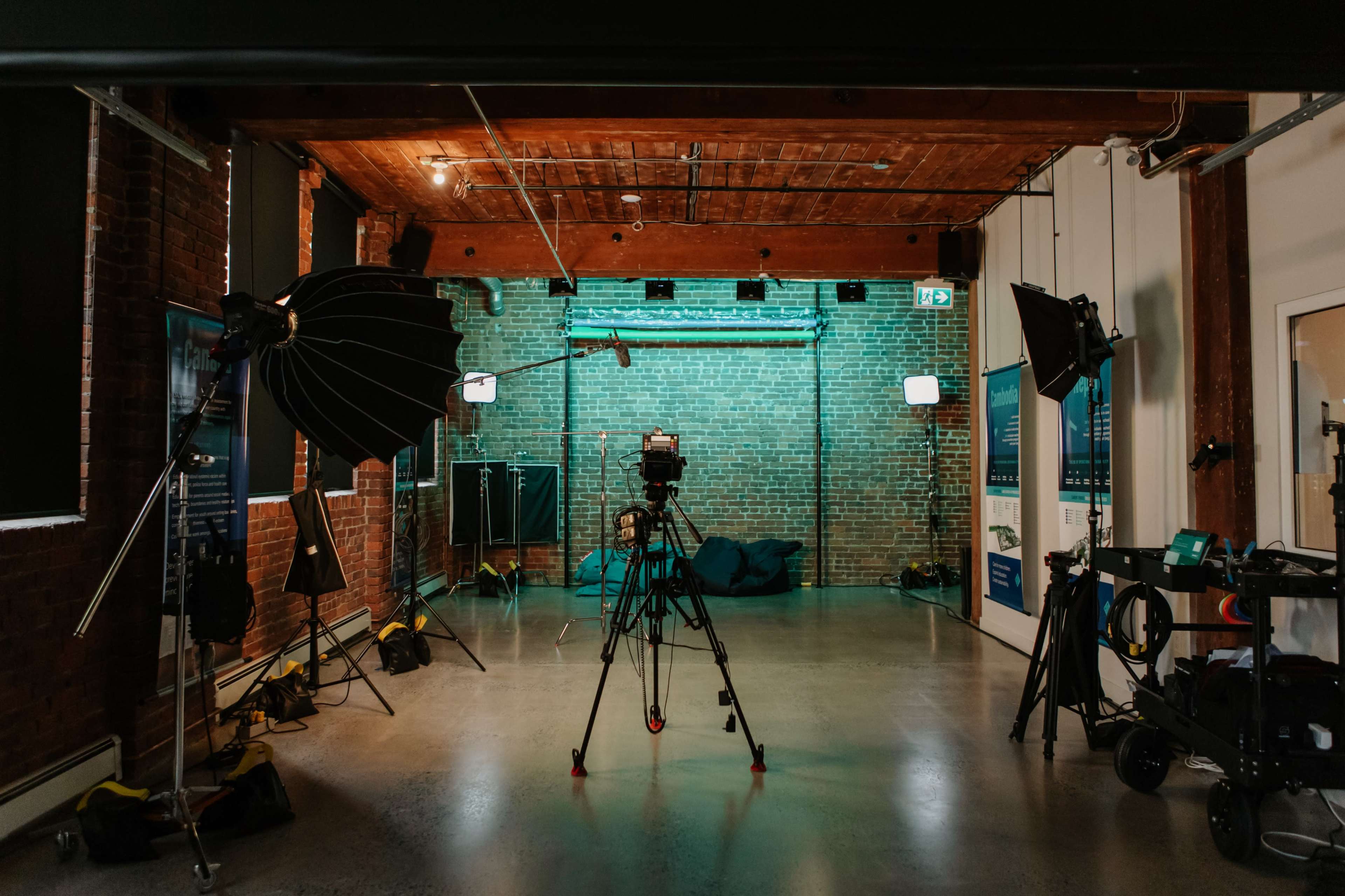A photography studio is set up with a camera on a tripod, softboxes, and a backdrop against a brick wall.