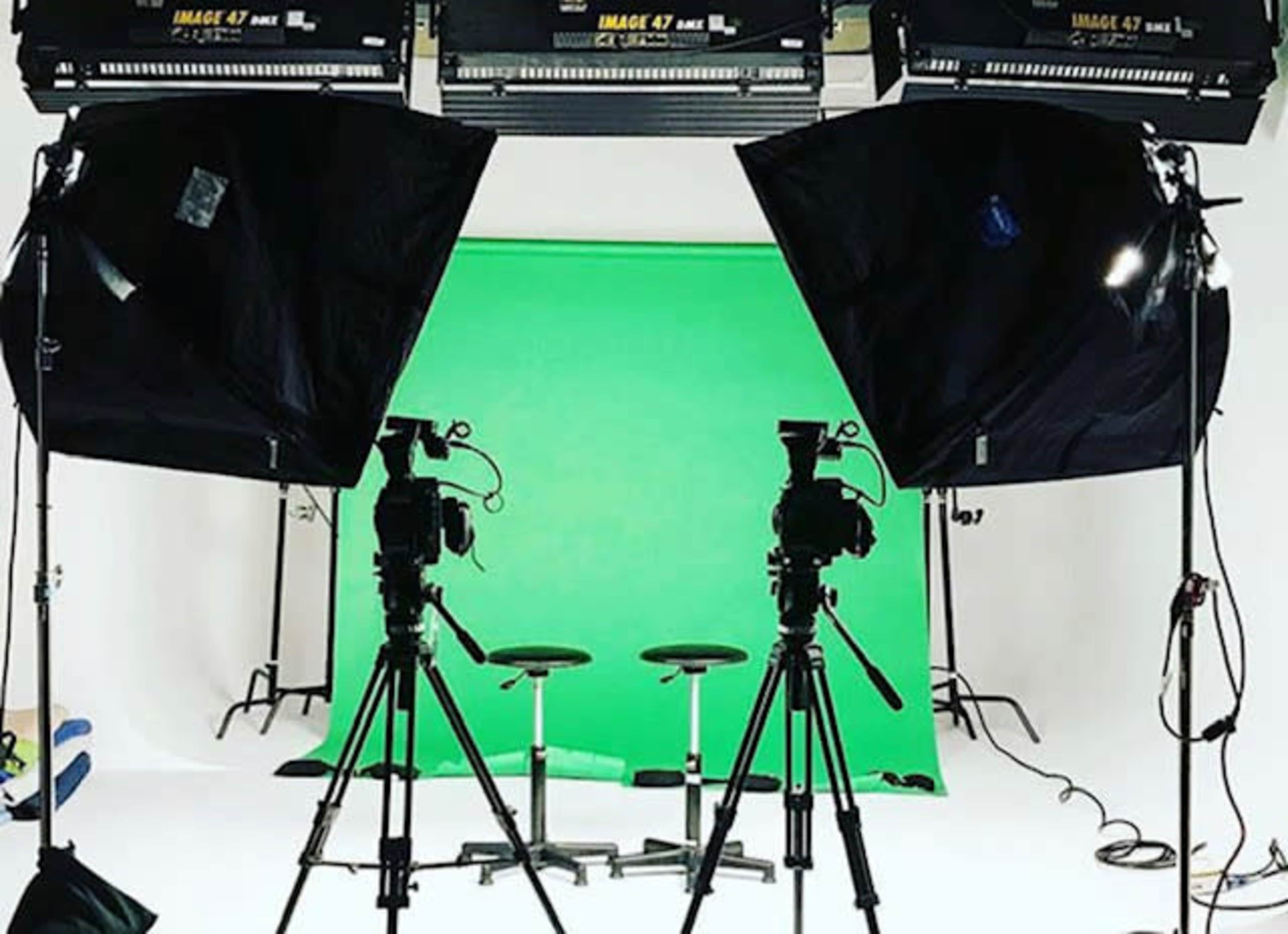 The image shows a photography studio setup with two cameras facing two black stools against a green backdrop, illuminated by softbox lights.