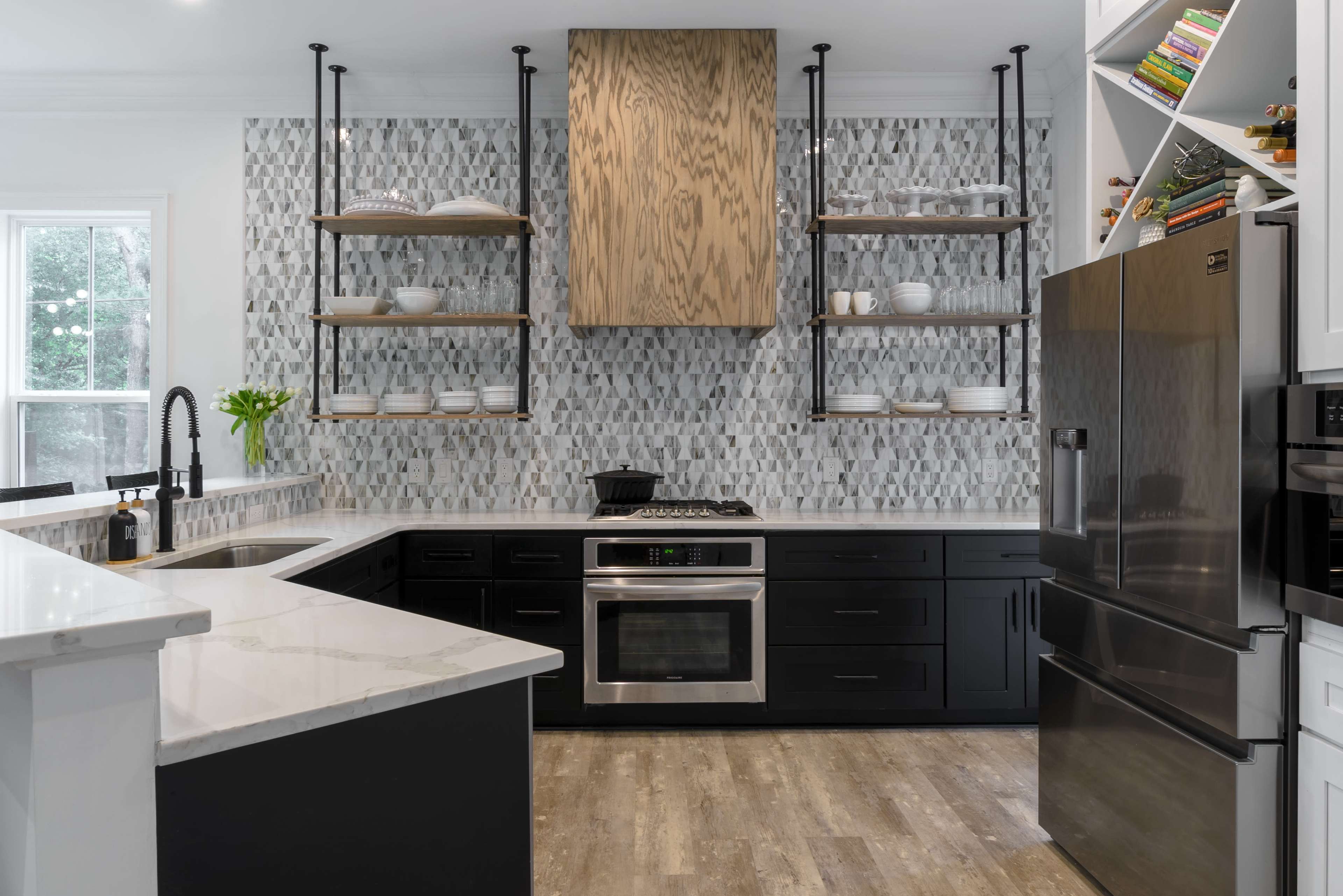 The image shows a modern kitchen featuring black cabinetry, open shelving with decorative items, a stainless steel oven, and a marble countertop.