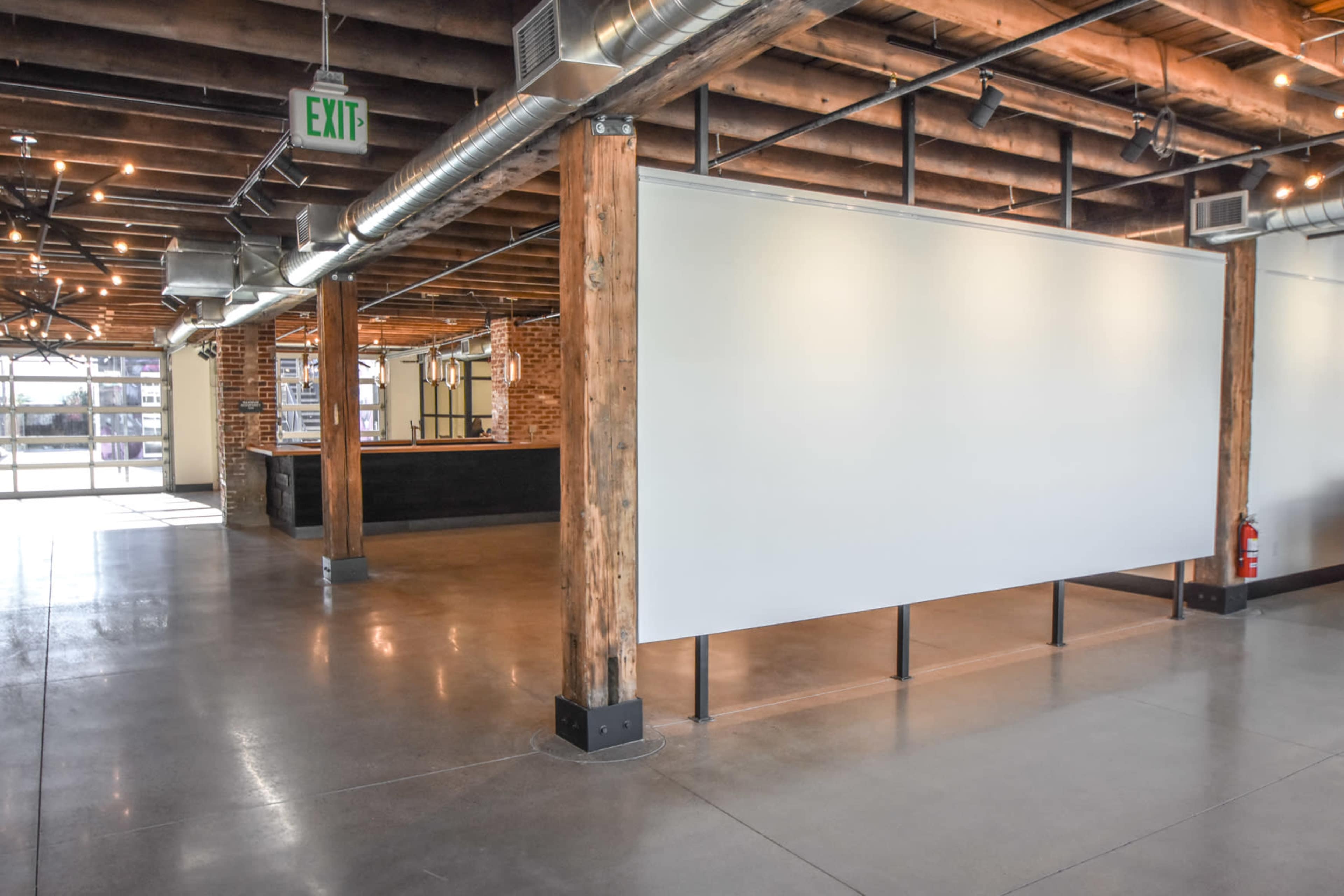 An industrial-style interior with exposed wooden beams, concrete flooring, and a partitioned area that separates a bar counter from an open space.