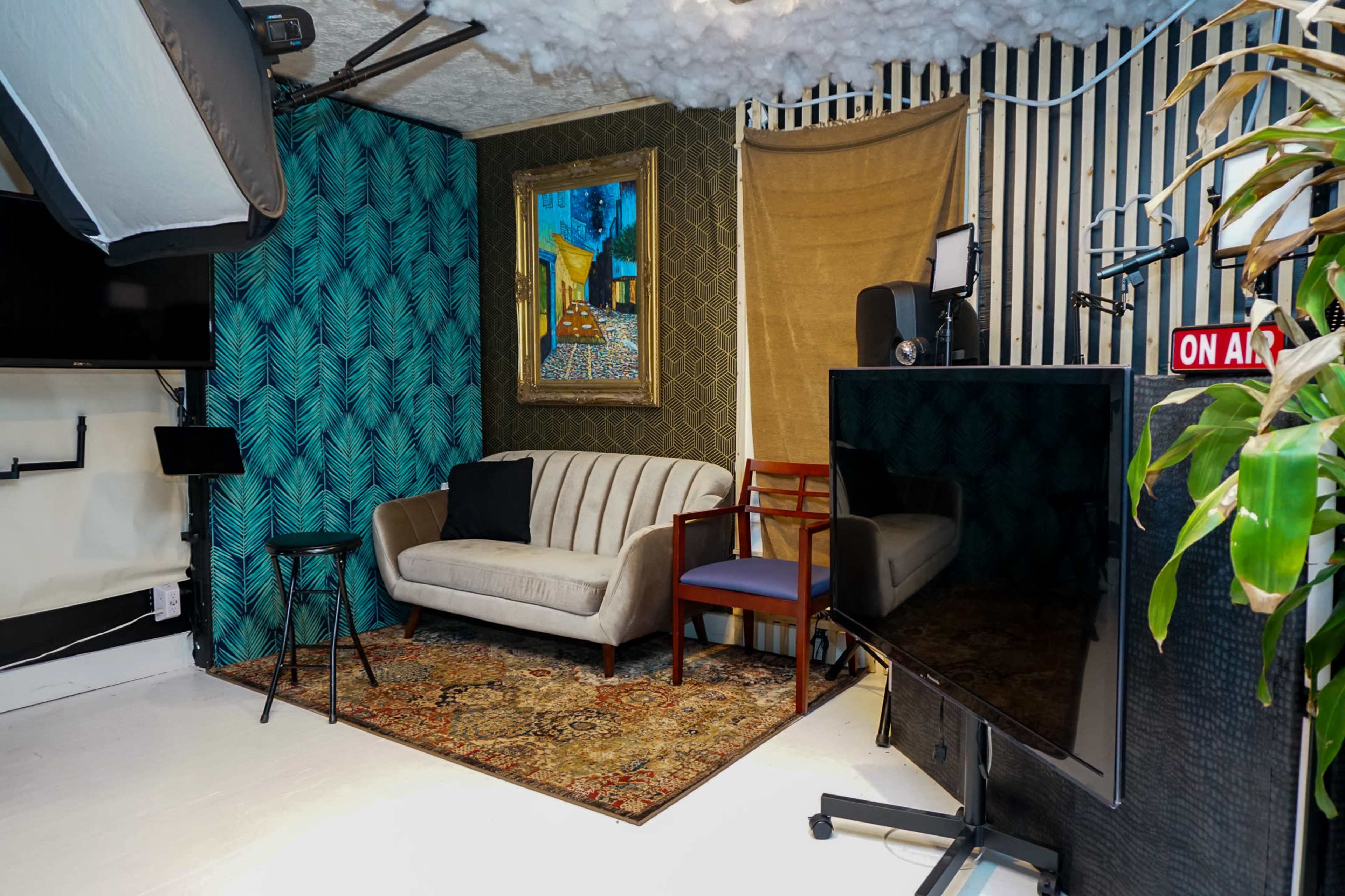The image shows a cozy recording studio featuring a striped wall, a painting, a patterned rug, a sofa, a chair, and a large television.