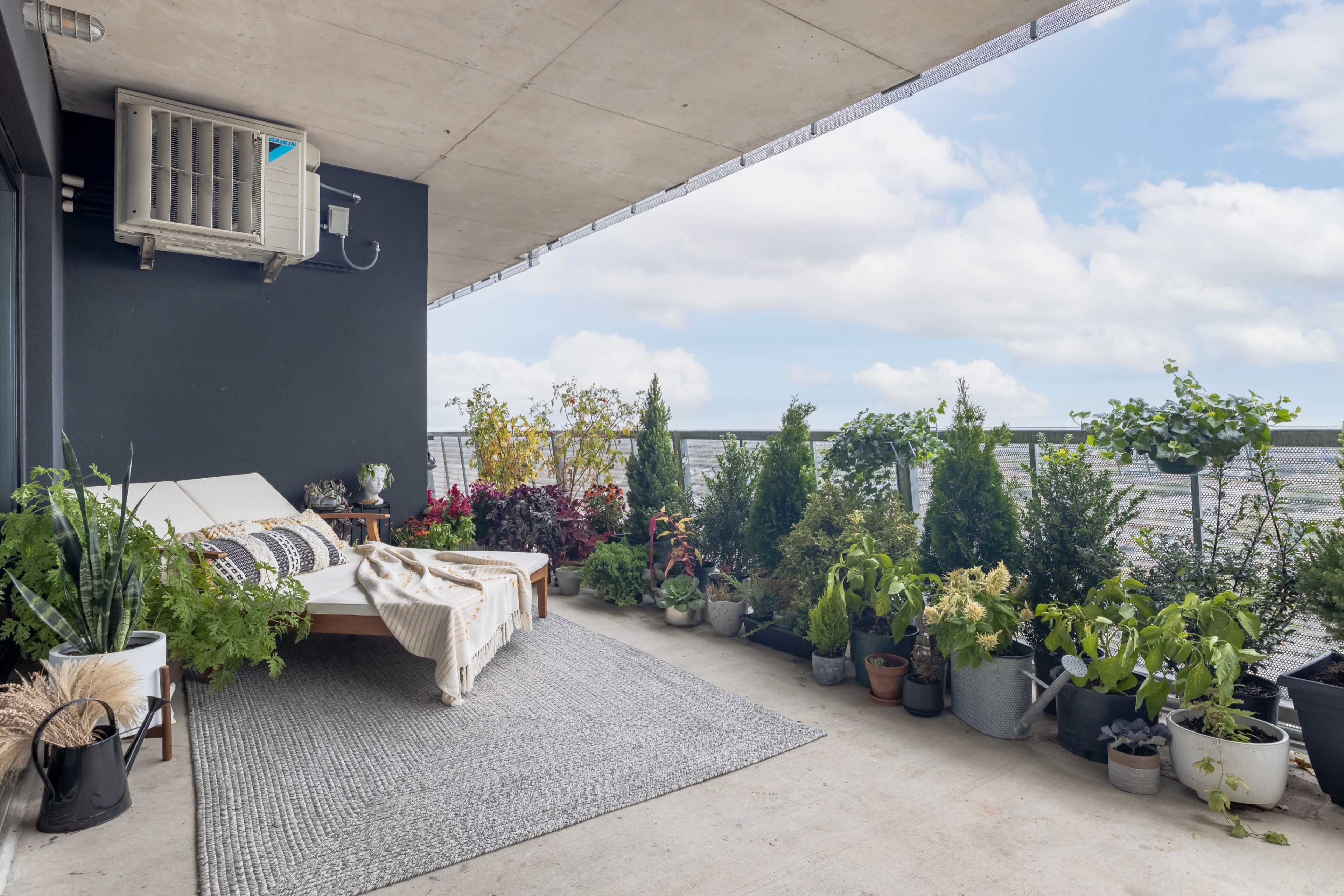 A balcony features a seating area with a daybed and numerous potted plants along the railing.