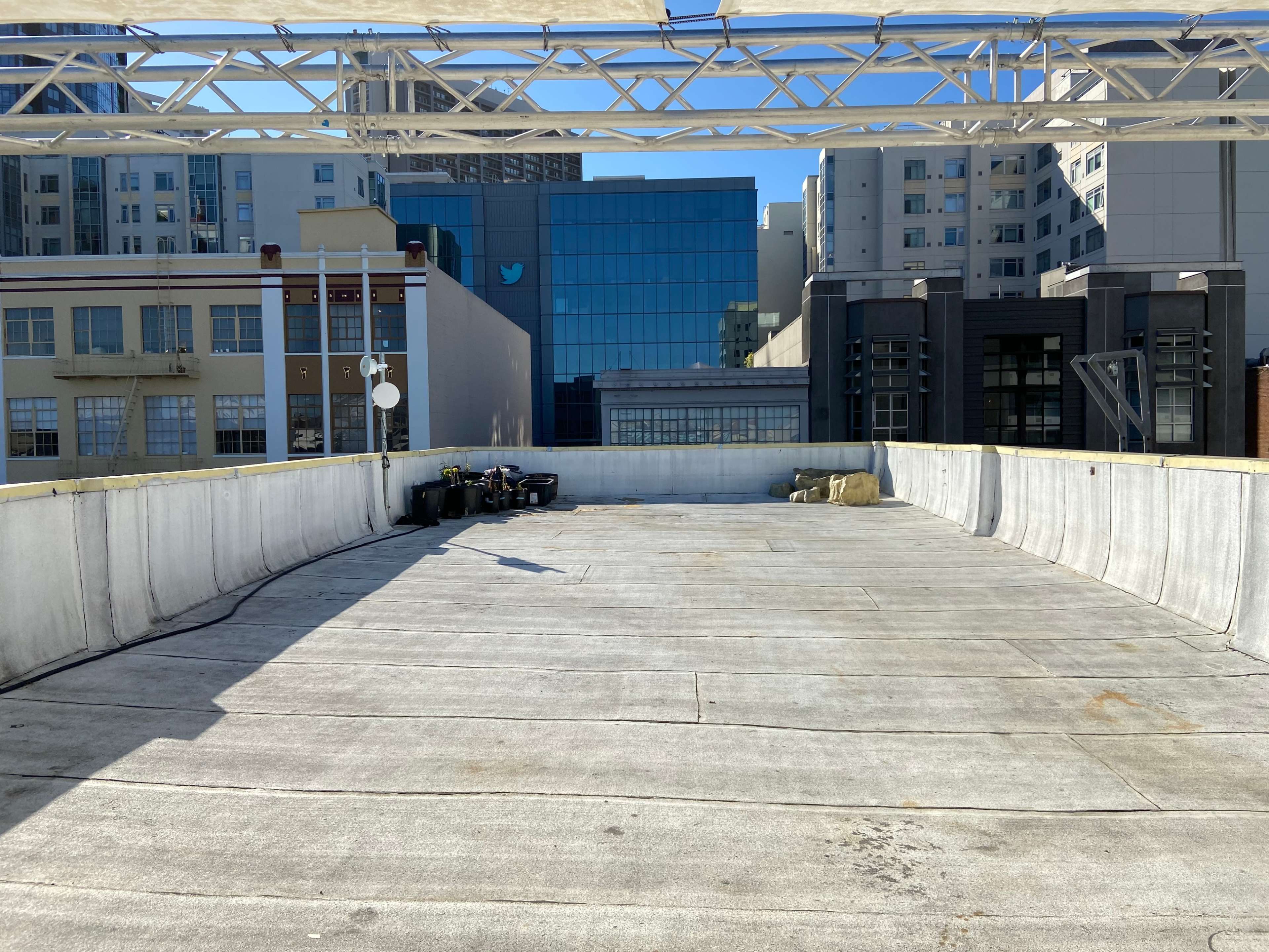 A large, empty rooftop space with concrete flooring and a skyline featuring multistory buildings, including one with the Twitter logo.