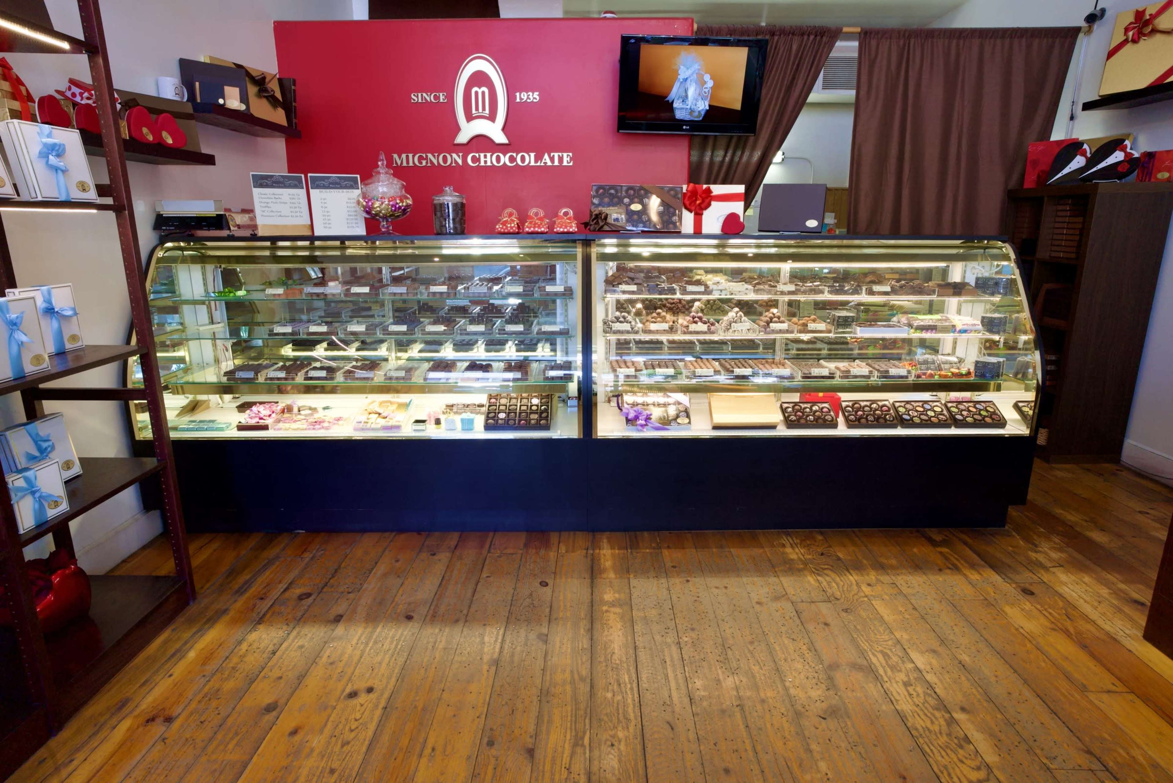 The image shows the interior of a chocolate shop with a display case filled with various types of chocolates and confections.