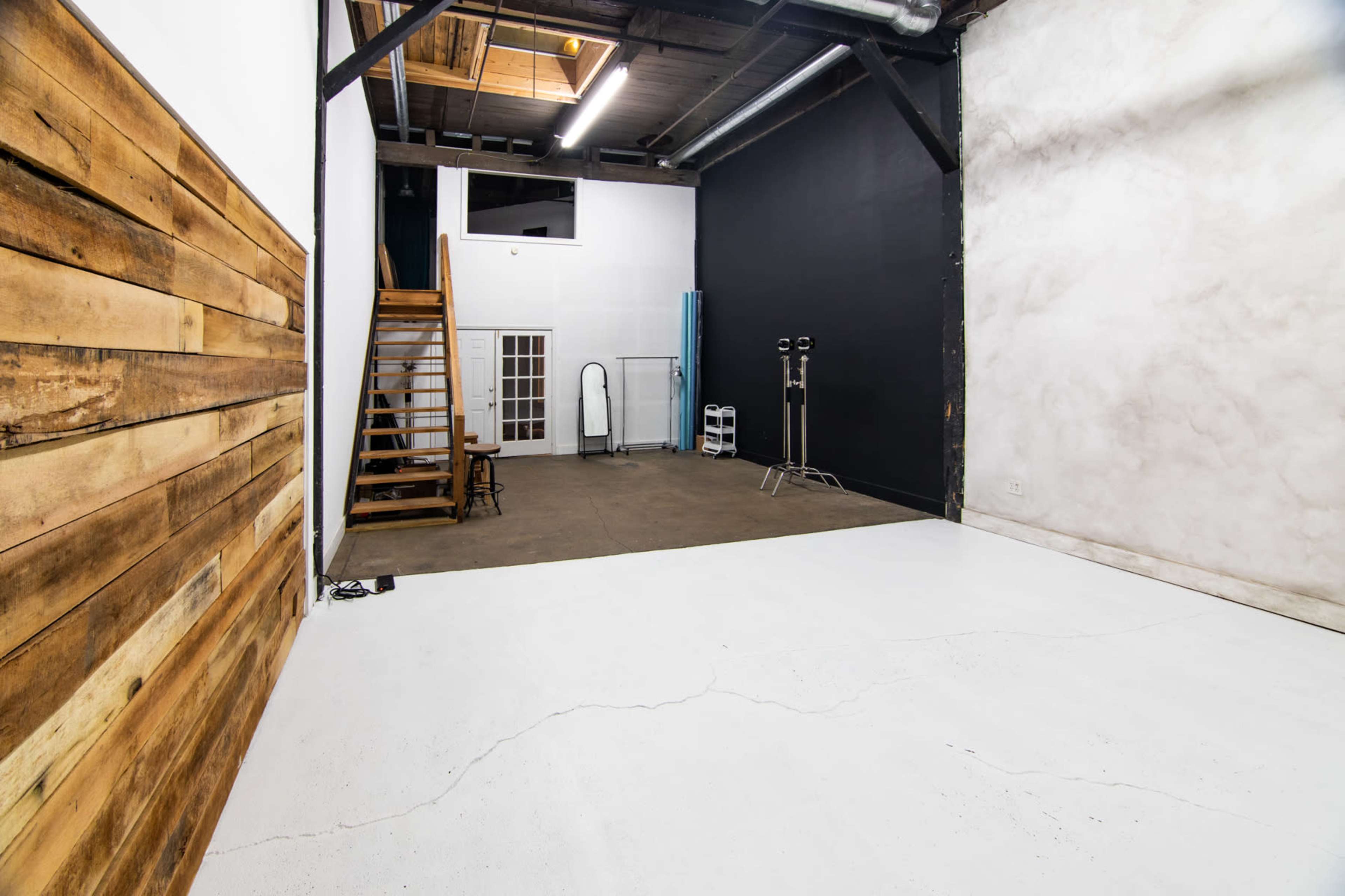 An empty studio space featuring wooden walls, a black wall, and a staircase leading to an upper level.