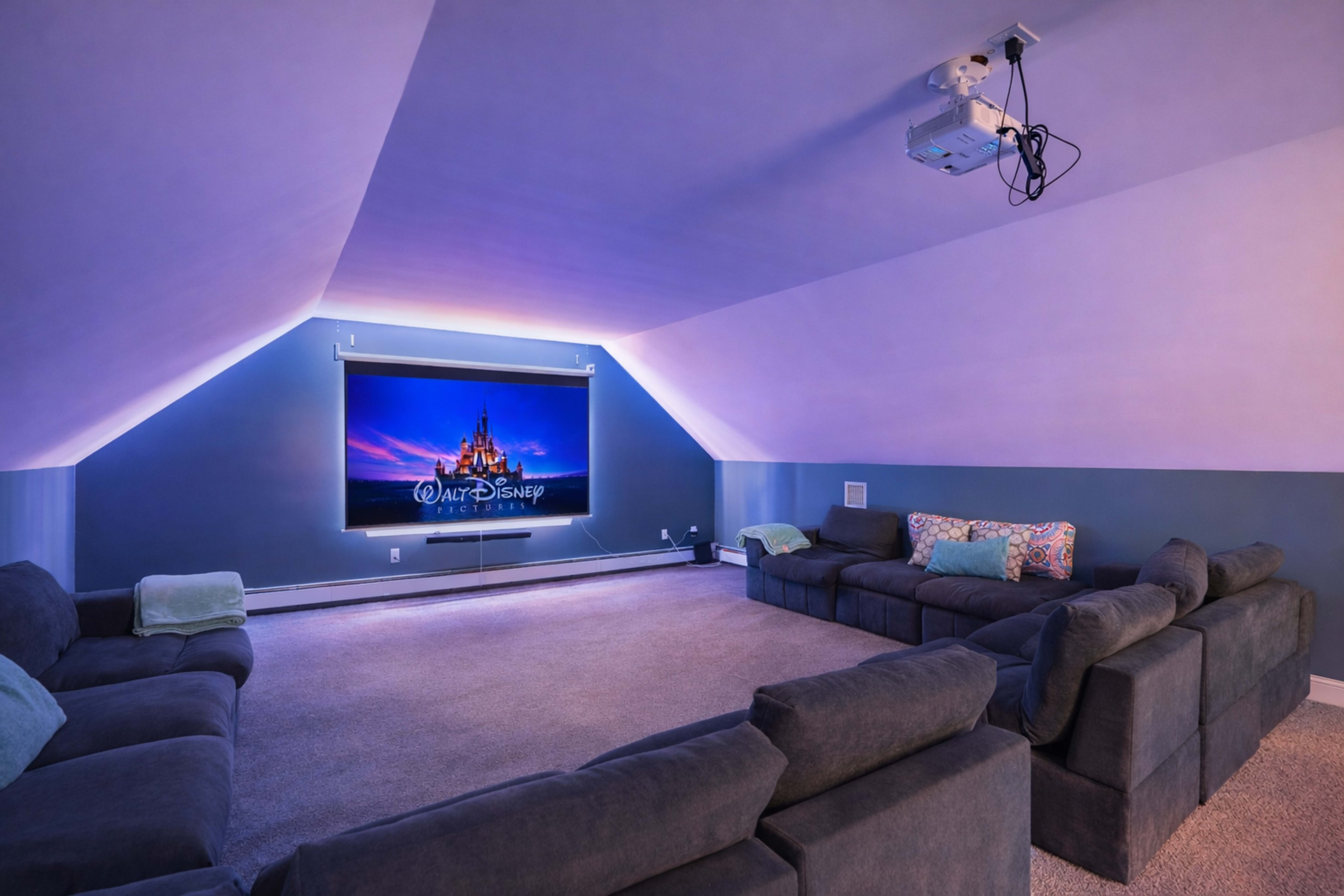 A cozy home theater features a large screen displaying the Walt Disney logo, with seating arranged in a circular layout around the room.