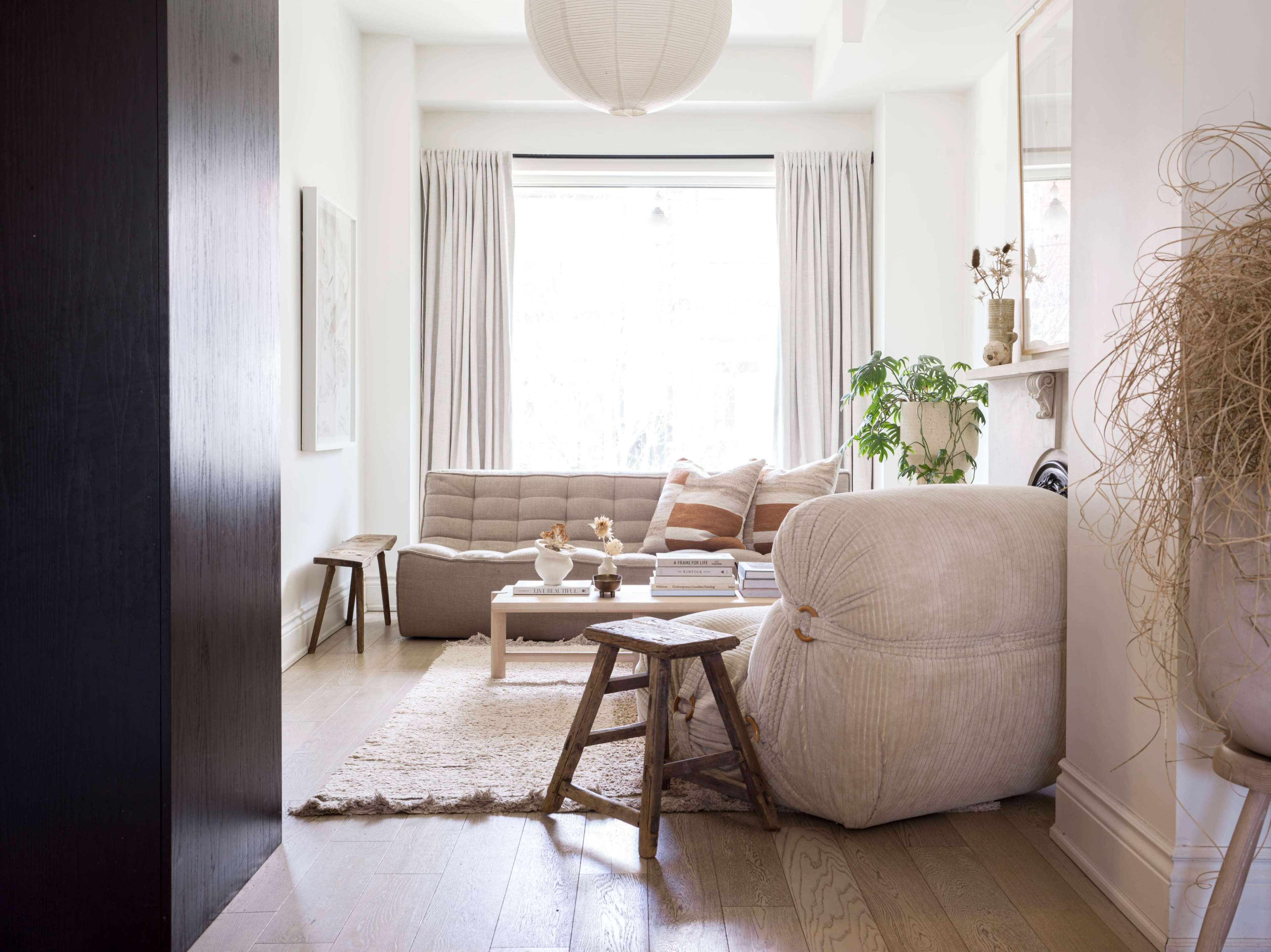 A light-colored living room with a sofa, a round coffee table, and a large floor cushion, all arranged around a soft rug under natural light from a window.