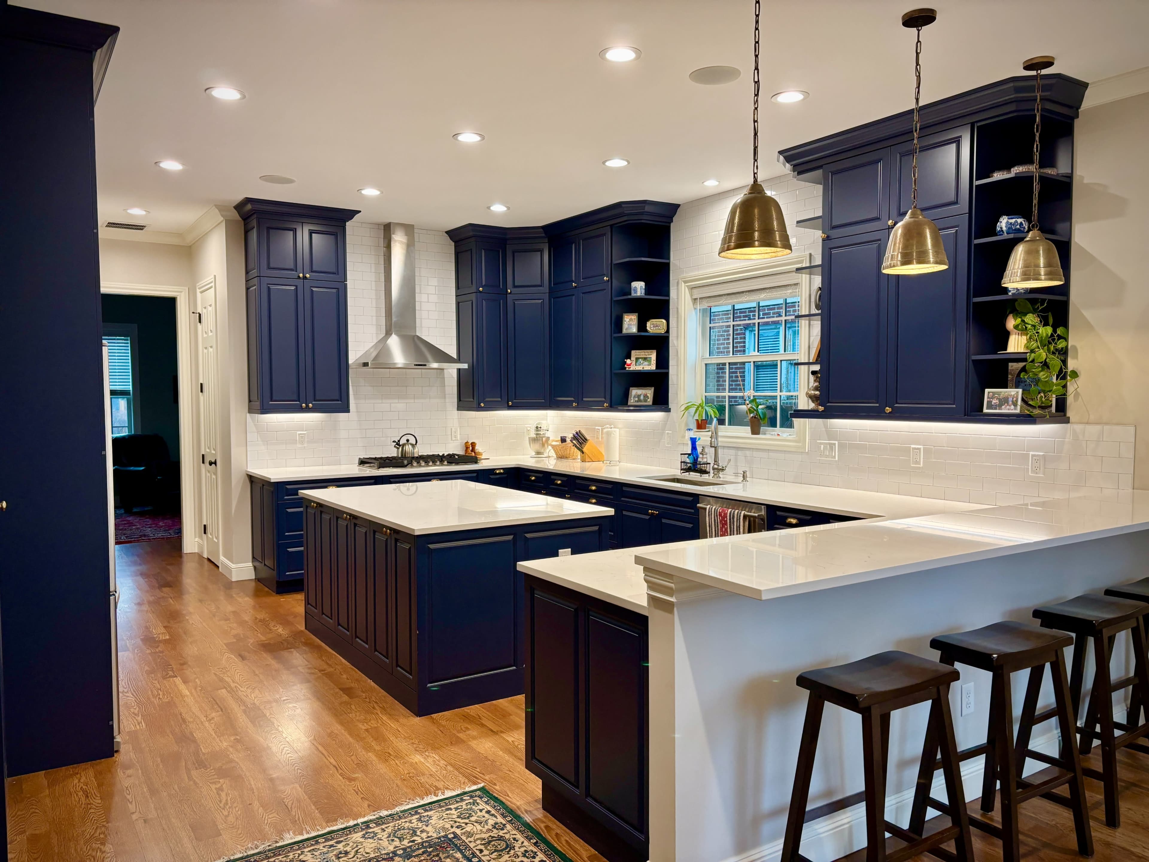 The kitchen features navy cabinets with white countertops, stainless steel appliances, and pendant lighting over a breakfast bar.