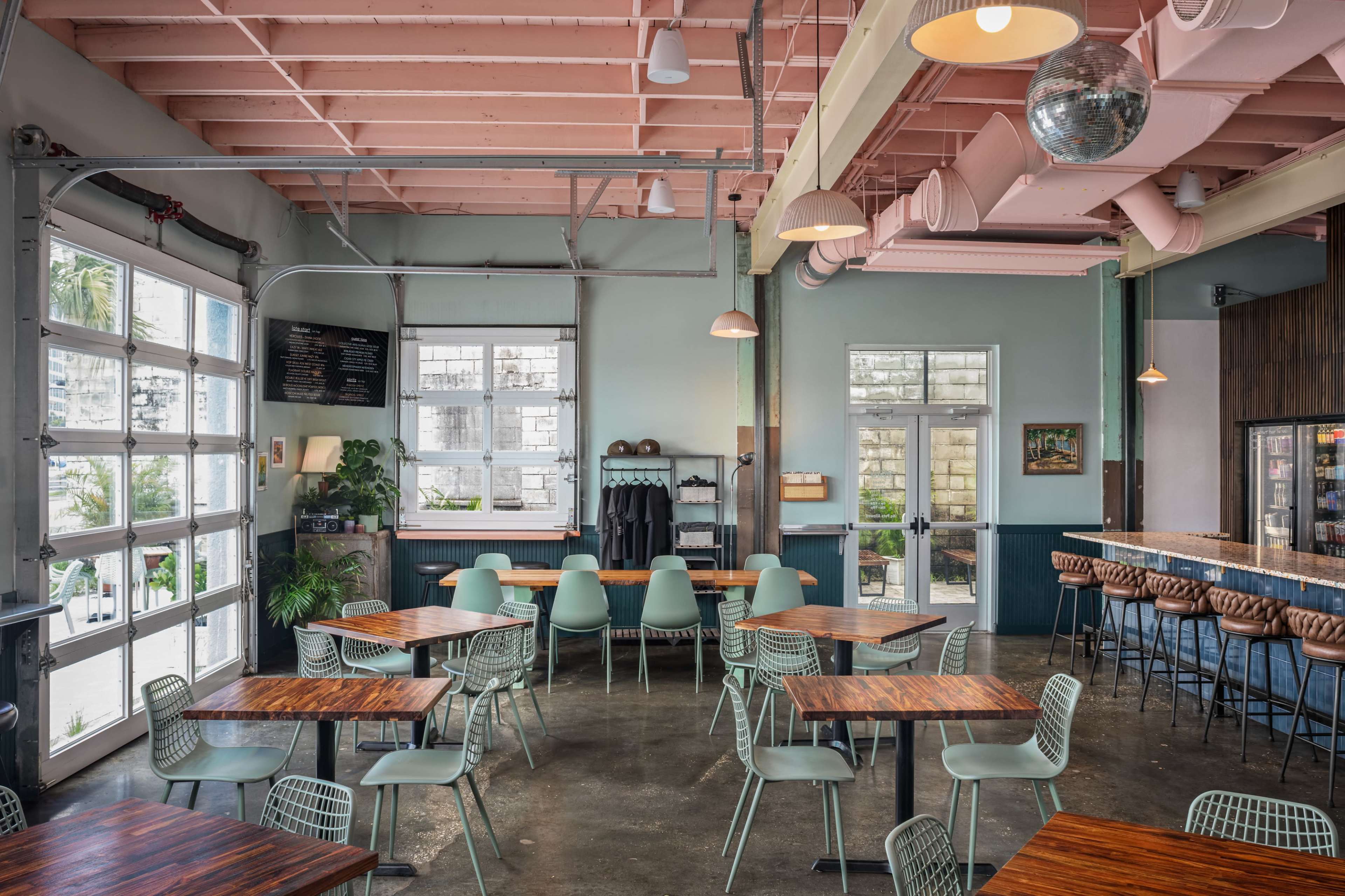 The interior of a modern restaurant features a combination of wooden tables, green chairs, and large windows that allow natural light to fill the space.