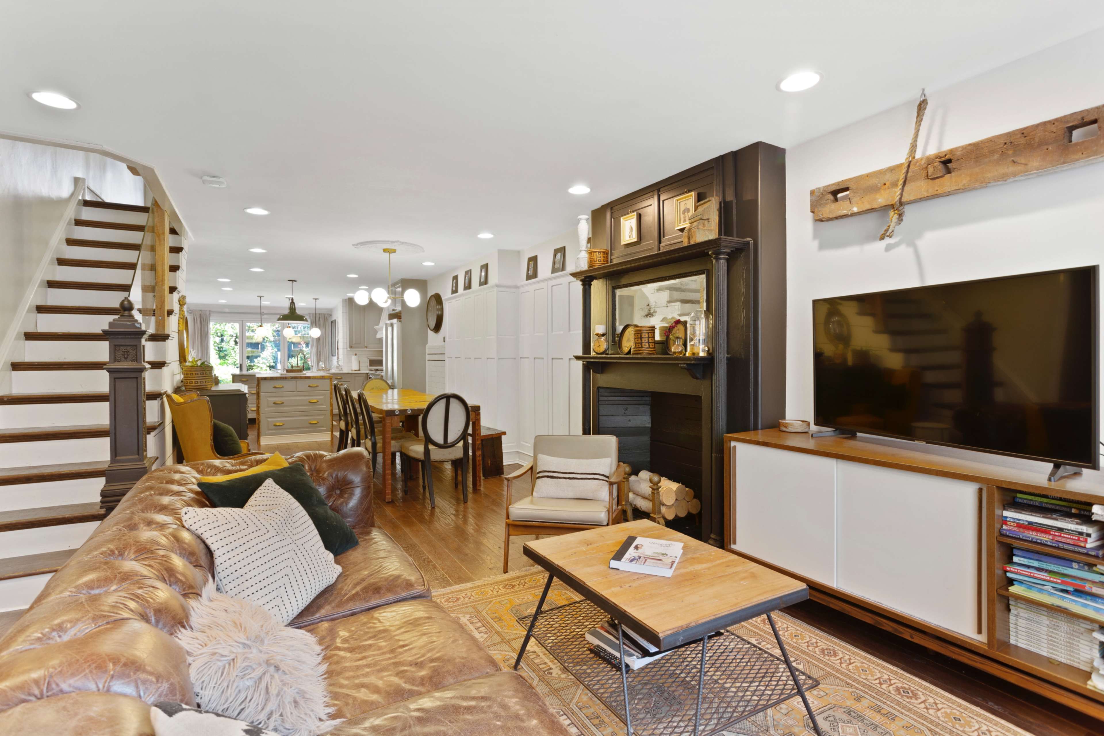 A modern living room featuring a leather sofa, a wooden coffee table, built-in shelving, and a staircase leading to an upper level.