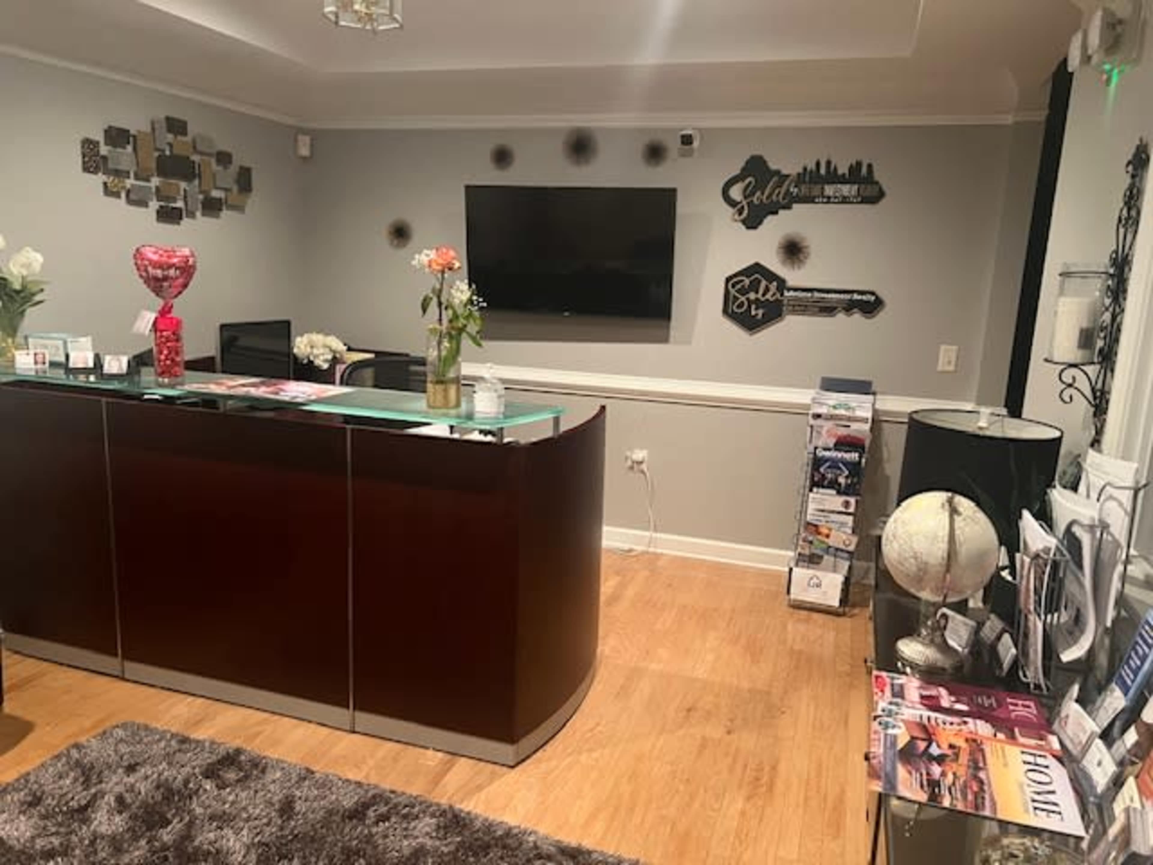 A reception area with a modern desk, a television on the wall, decorative wall art, and a globe on a side table.