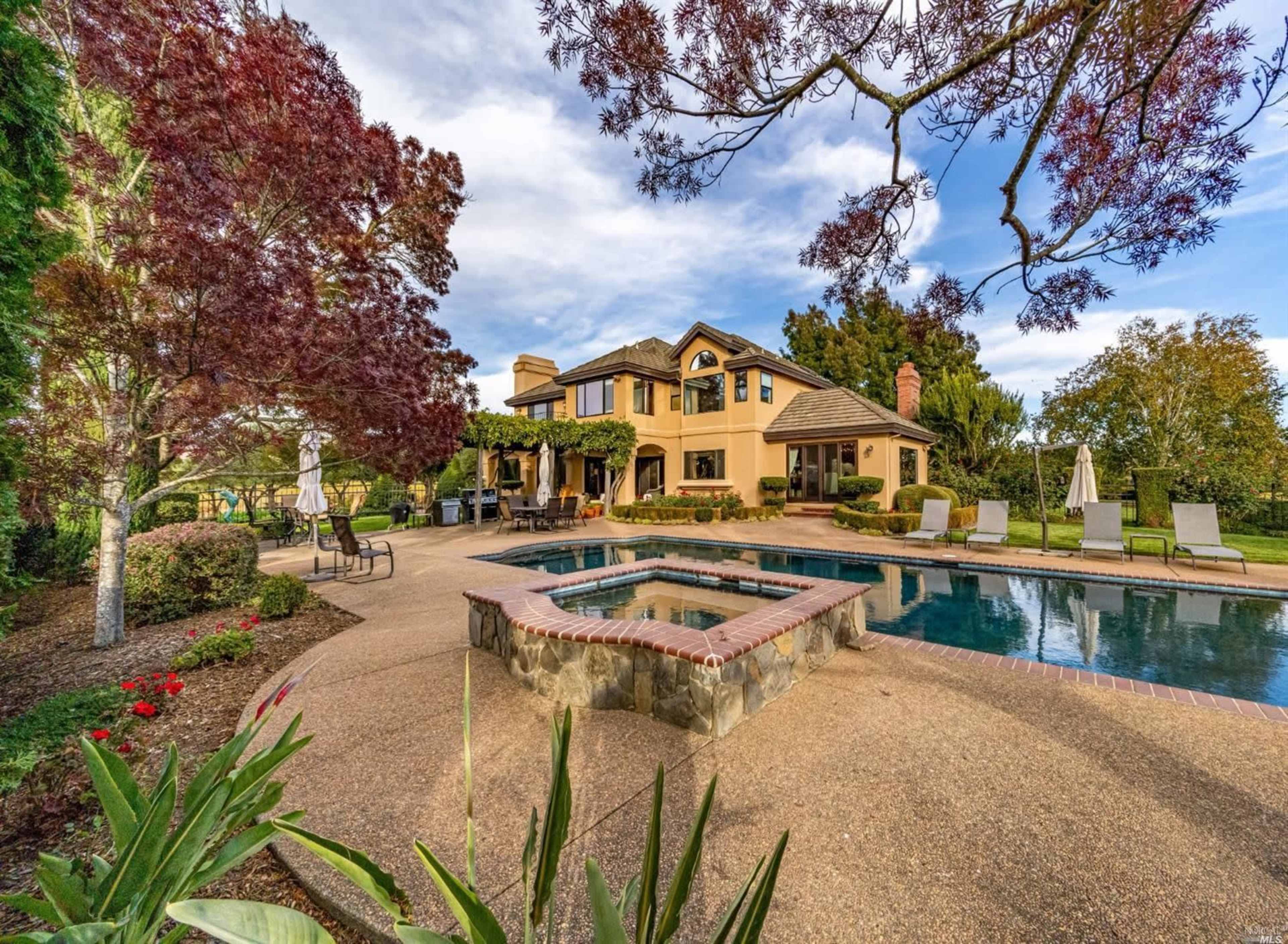 A landscaped backyard with a swimming pool and a two-story house surrounded by greenery and outdoor seating areas.