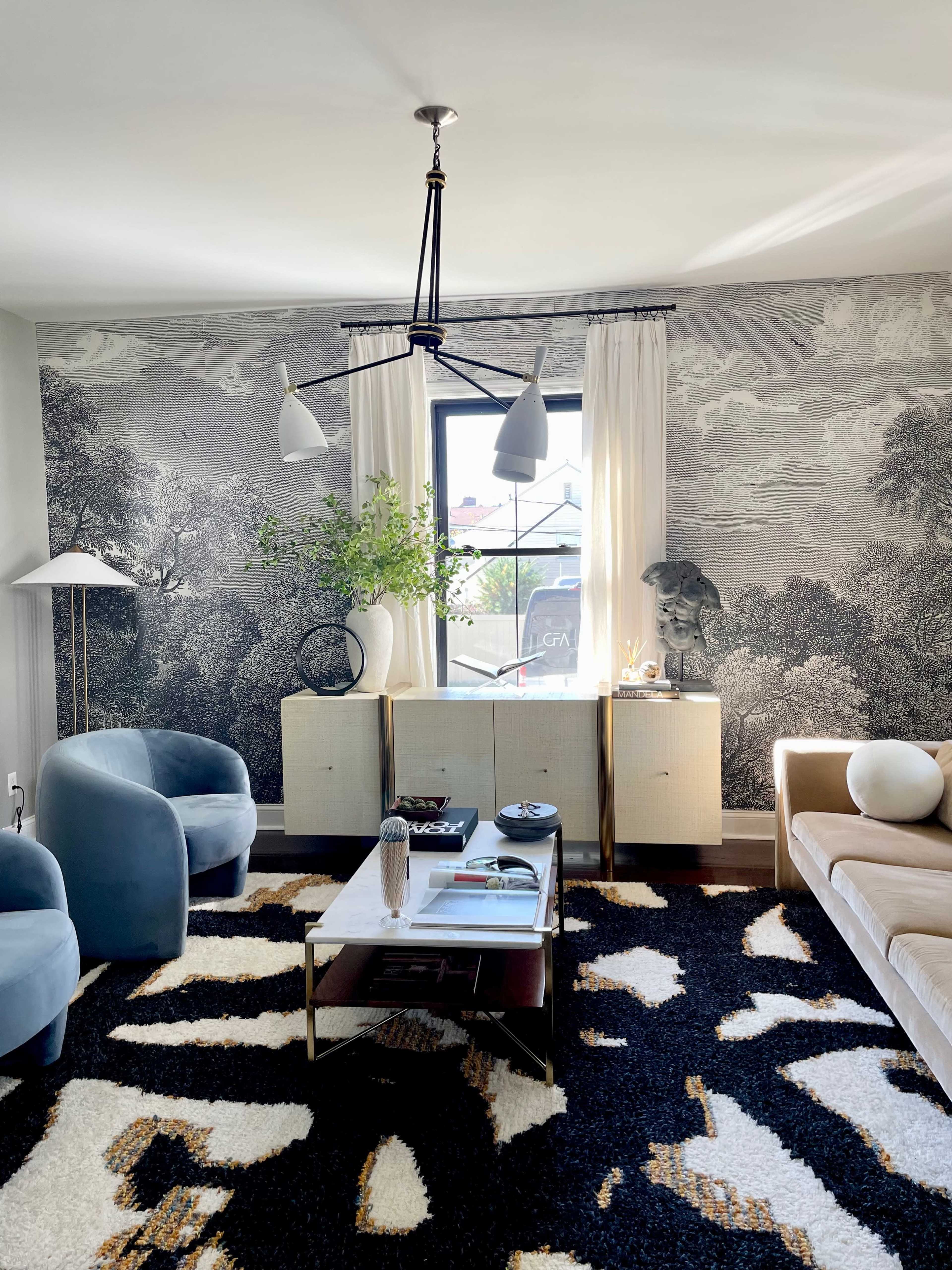 A modern living room featuring a patterned rug, a coffee table, a light fixture, and a large mural on the wall.