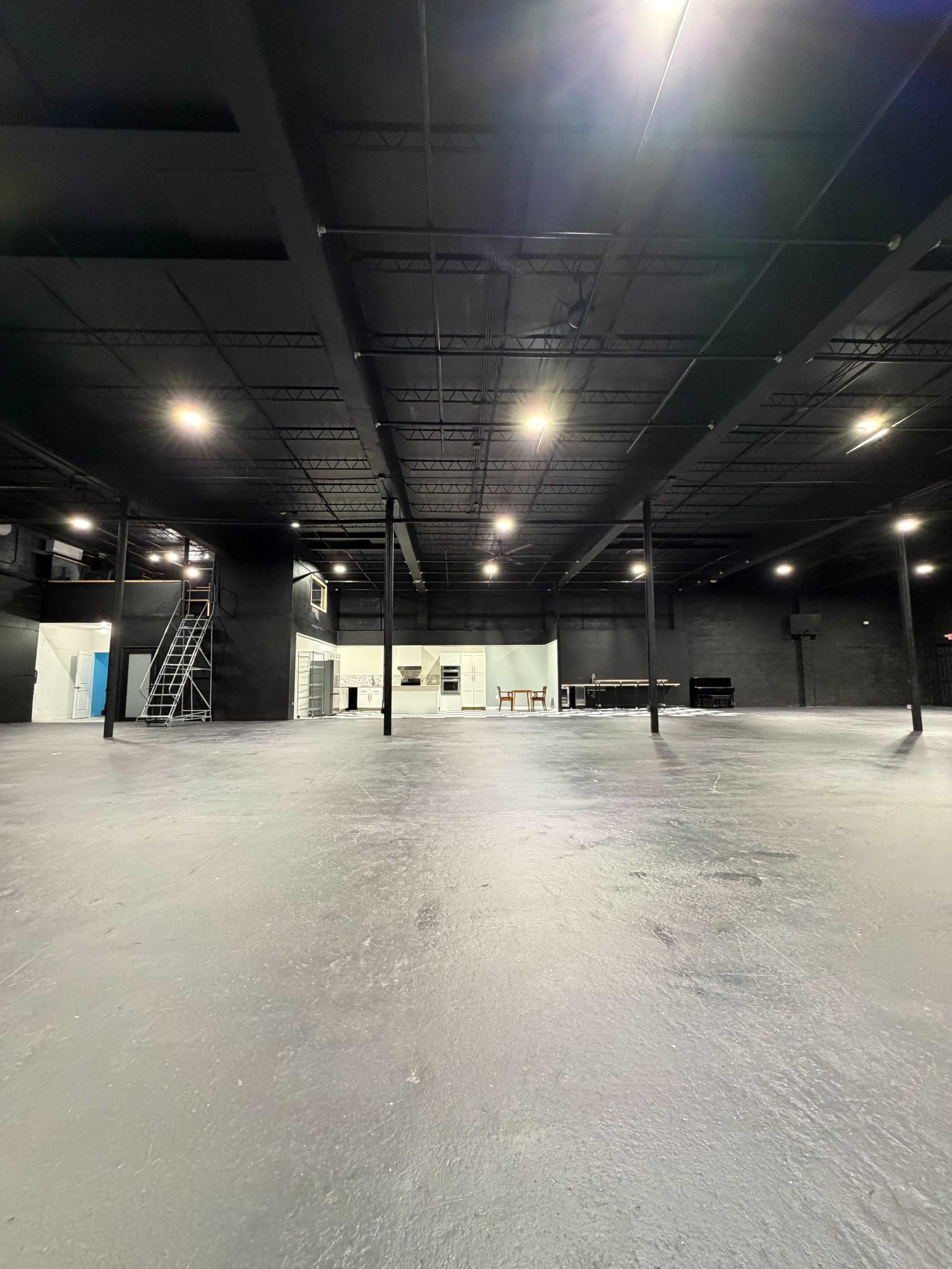 The image shows a large, empty warehouse-like space with black walls and a smooth gray floor, illuminated by overhead lights.