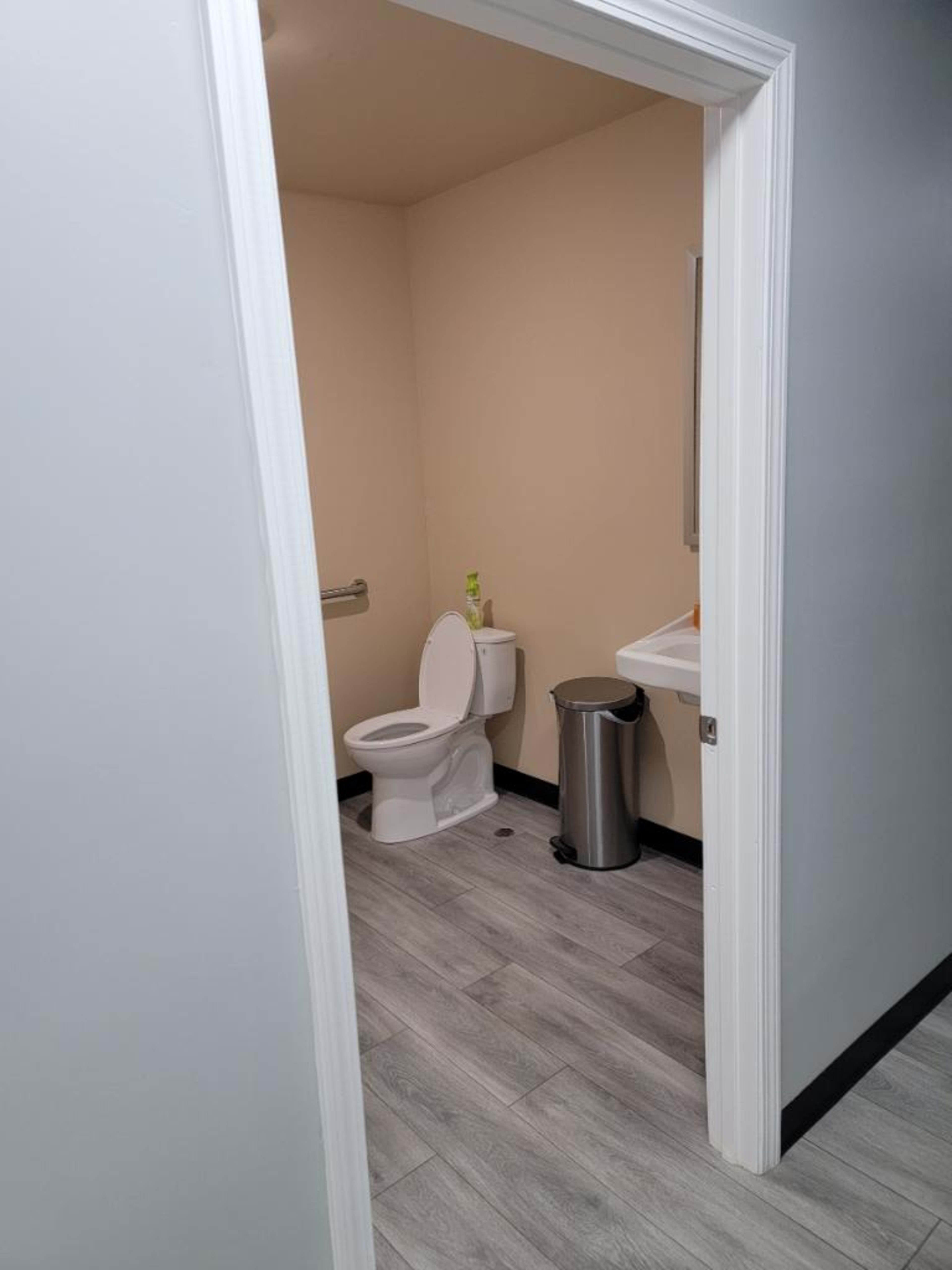 A view into a small restroom featuring a toilet, a sink, and a wastebasket on the floor.