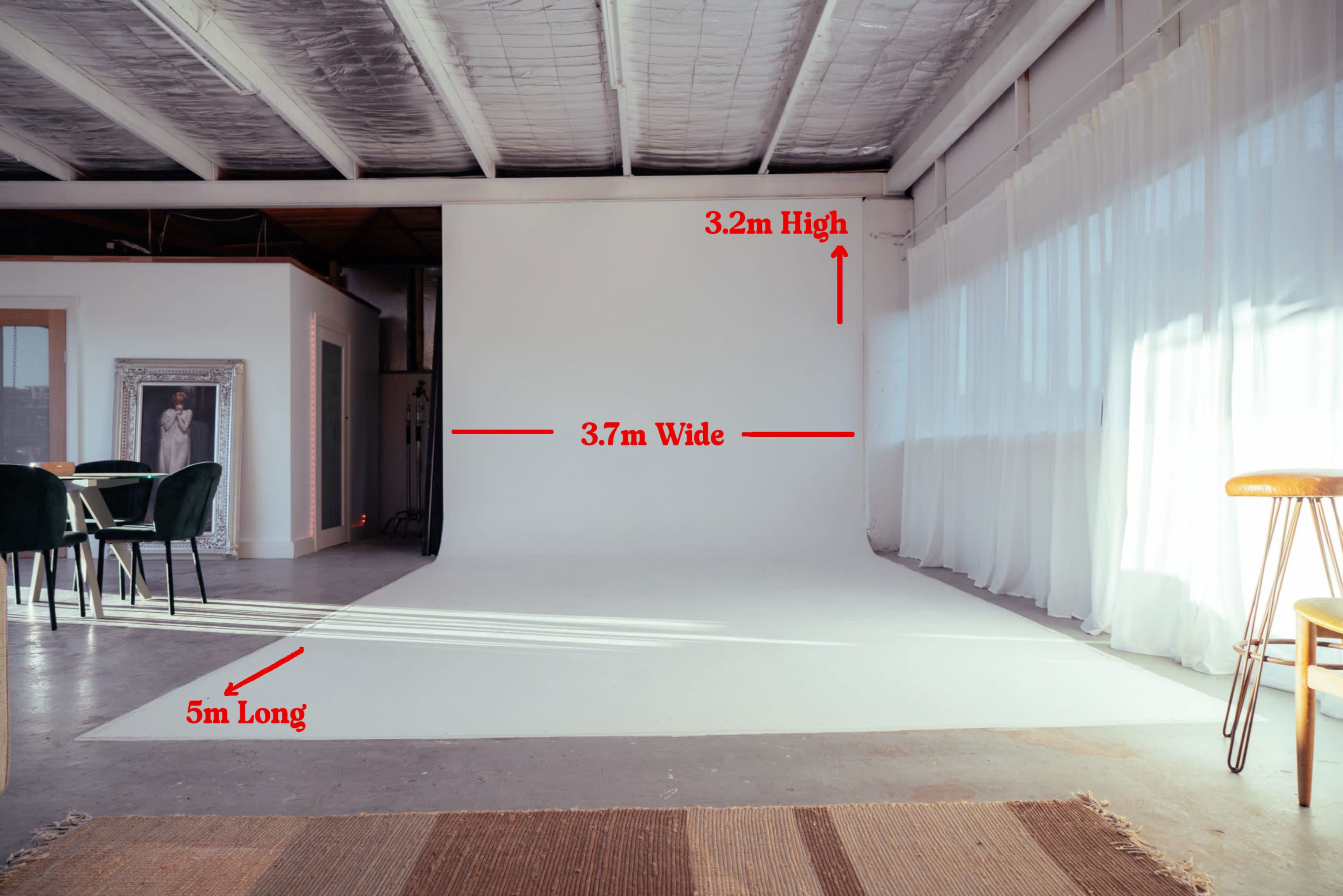 The image shows a spacious photography studio with a large white backdrop, measuring 3.2 meters high, 3.7 meters wide, and 5 meters long, alongside several furniture pieces.