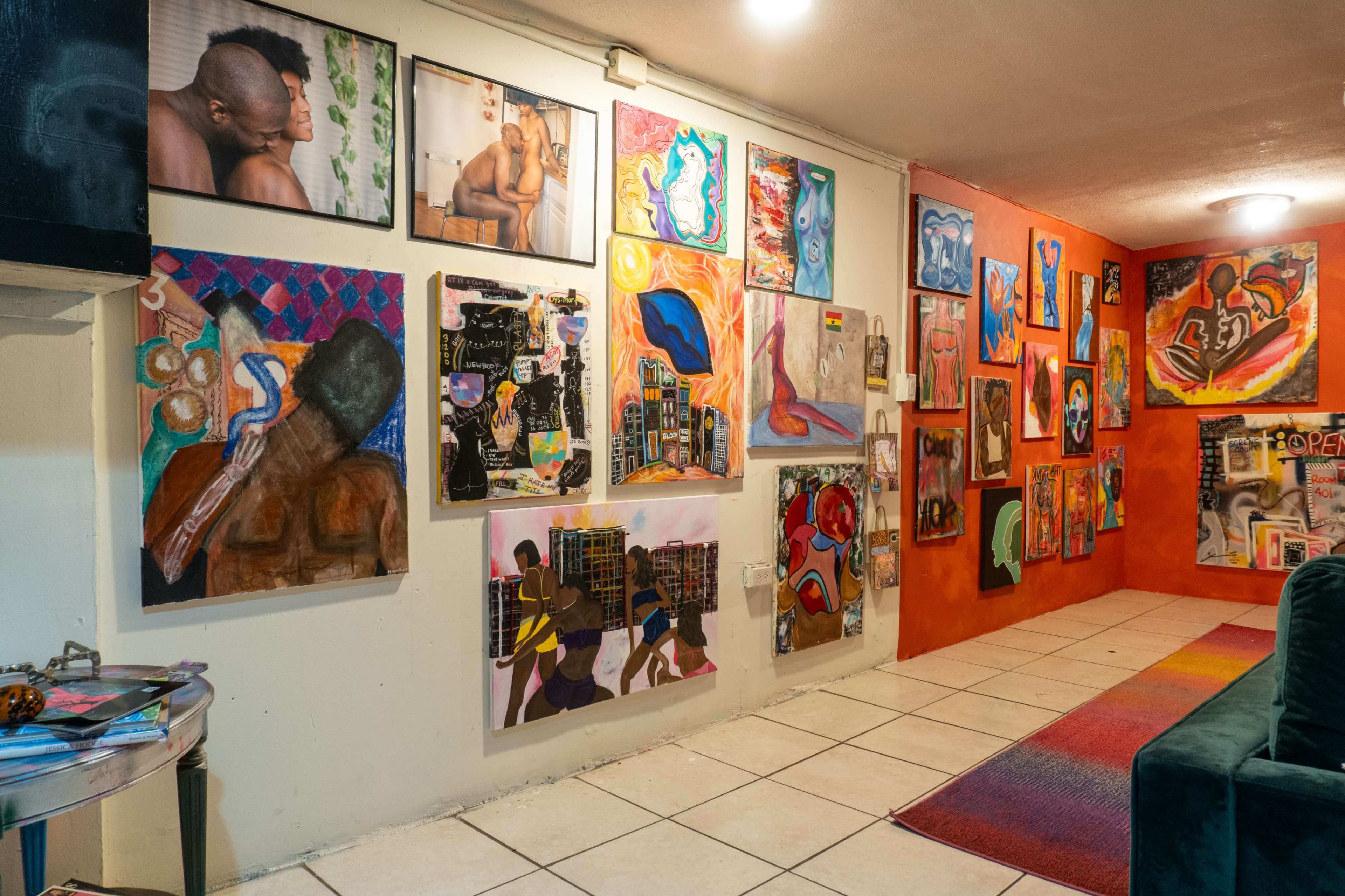 The image shows a colorful art gallery with various paintings displayed on the walls, featuring abstract and figurative artworks.