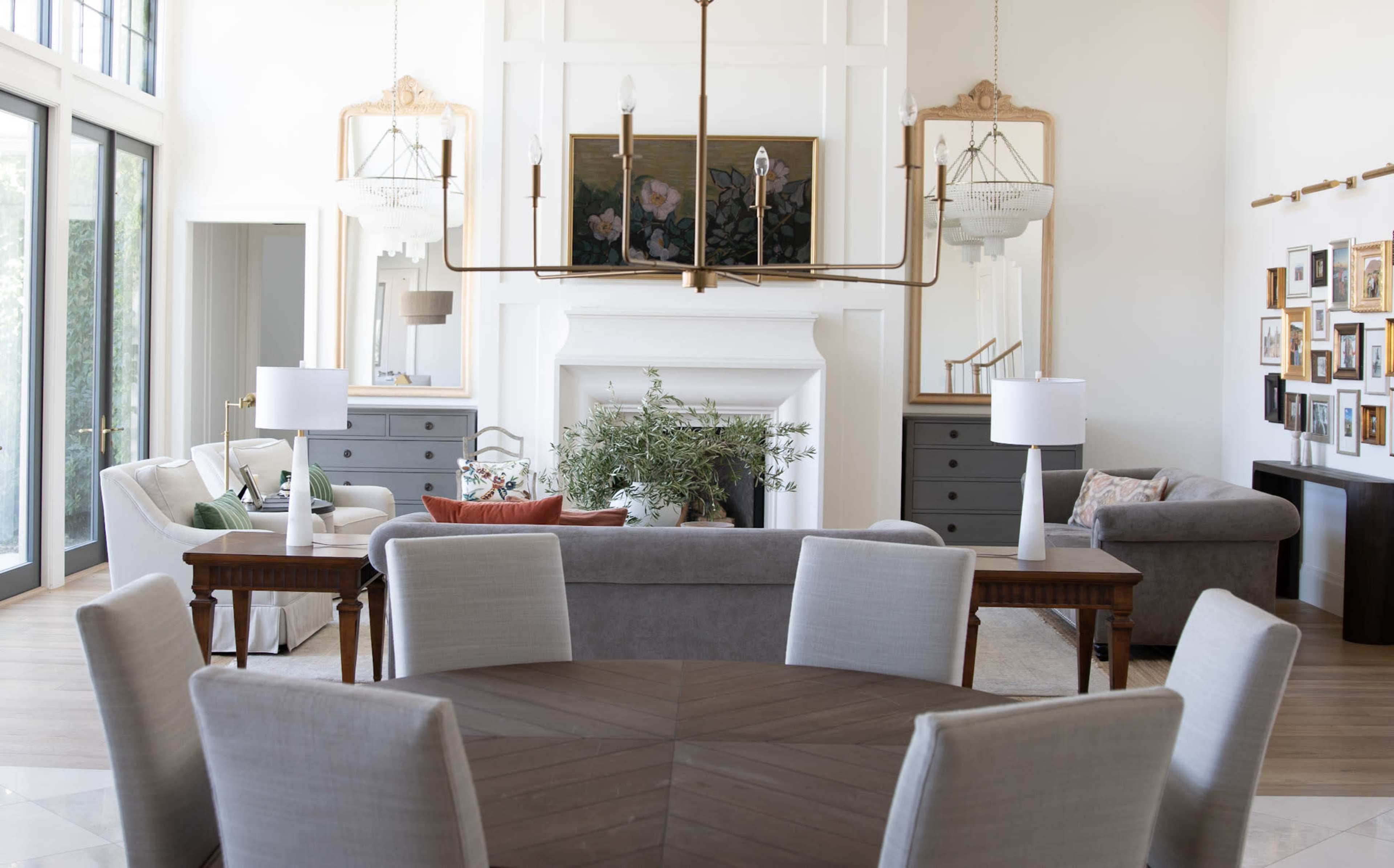 The image shows a bright and modern living room with a central dining table, a fireplace, and various seating areas arranged around it.