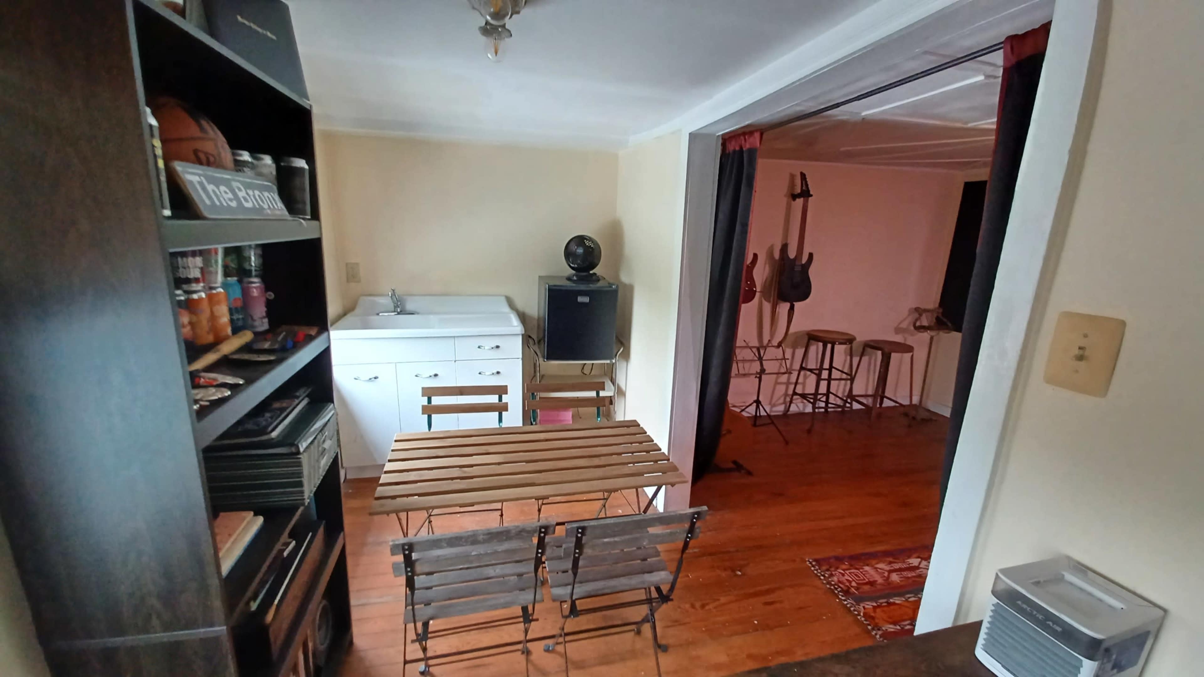 A small room with a washing machine and a dining table, leading to a space featuring musical instruments and barstools.