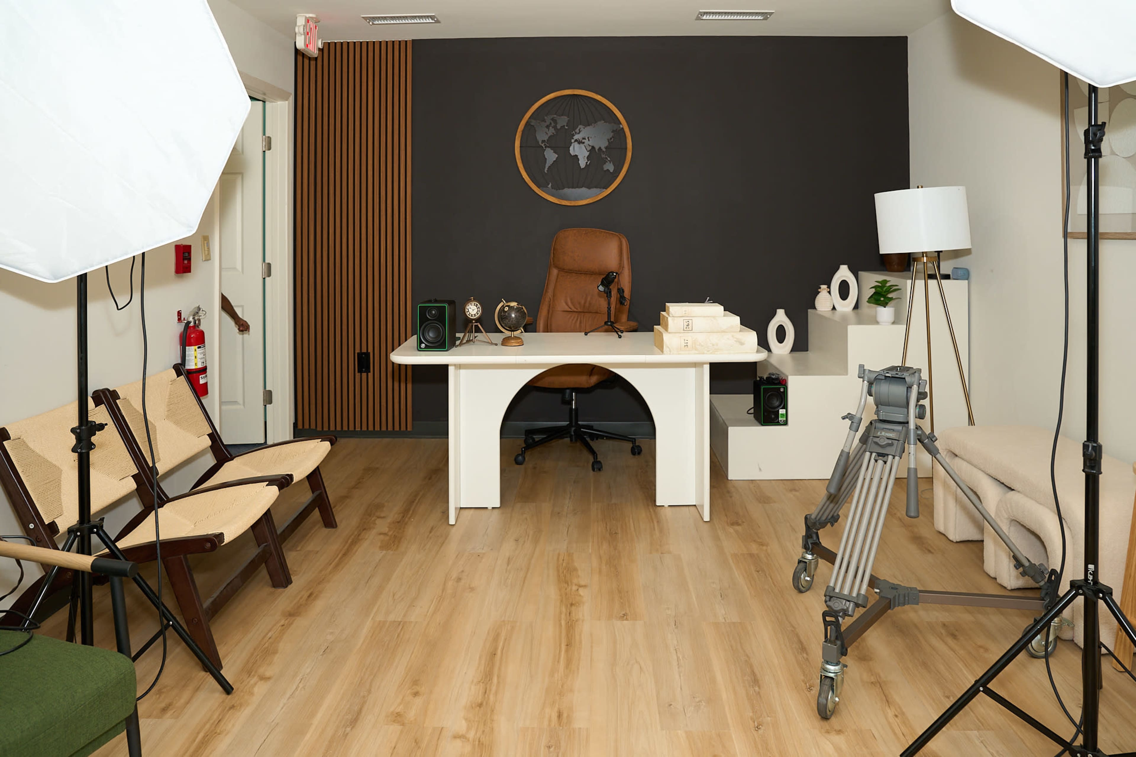 A modern office space features a large desk with a brown chair, wooden accents, and various decorative items, alongside a set of photography lights and director's equipment.