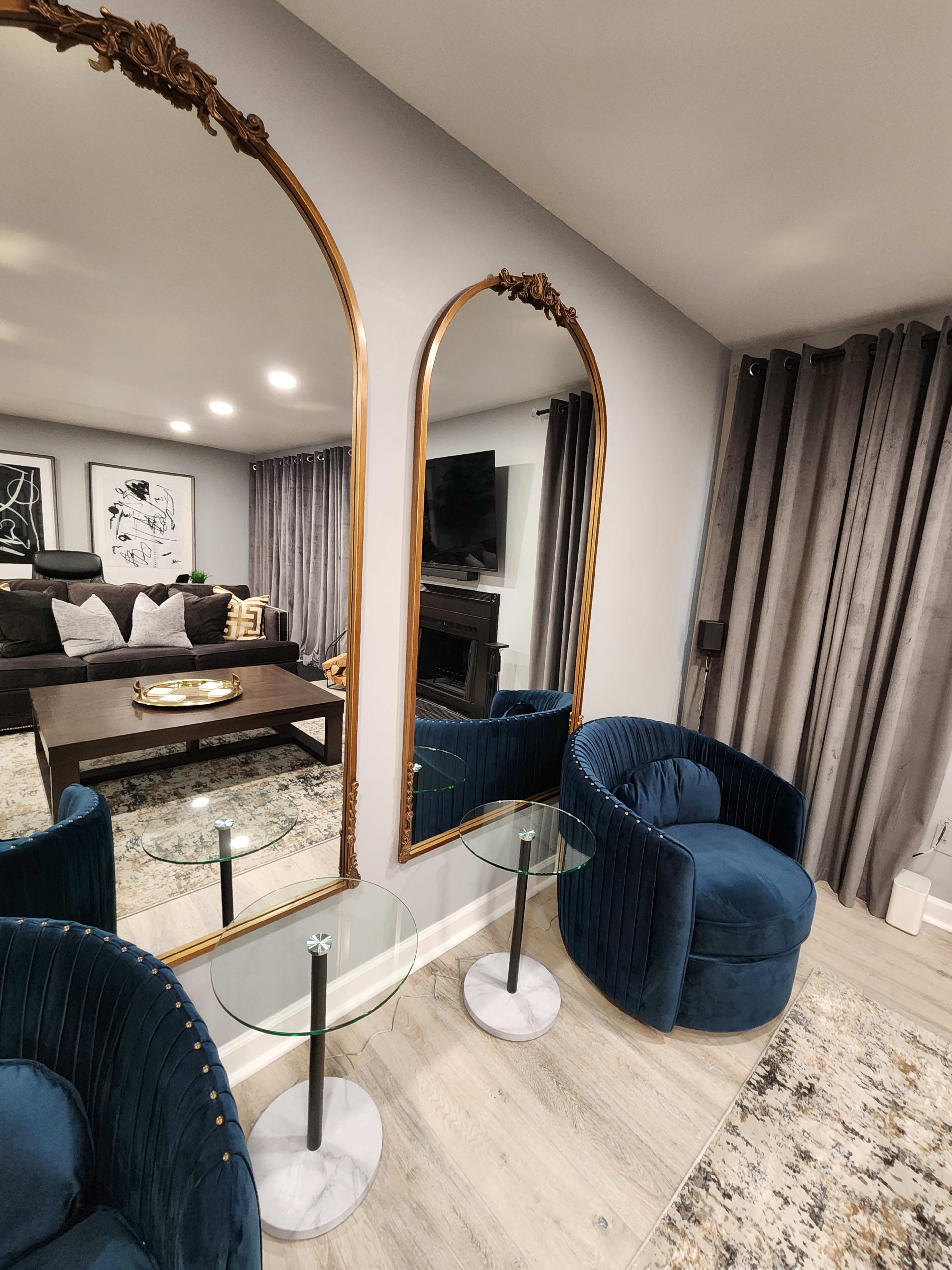 A living room with two ornate mirrors, a dark coffee table, and two blue armchairs beside glass side tables.