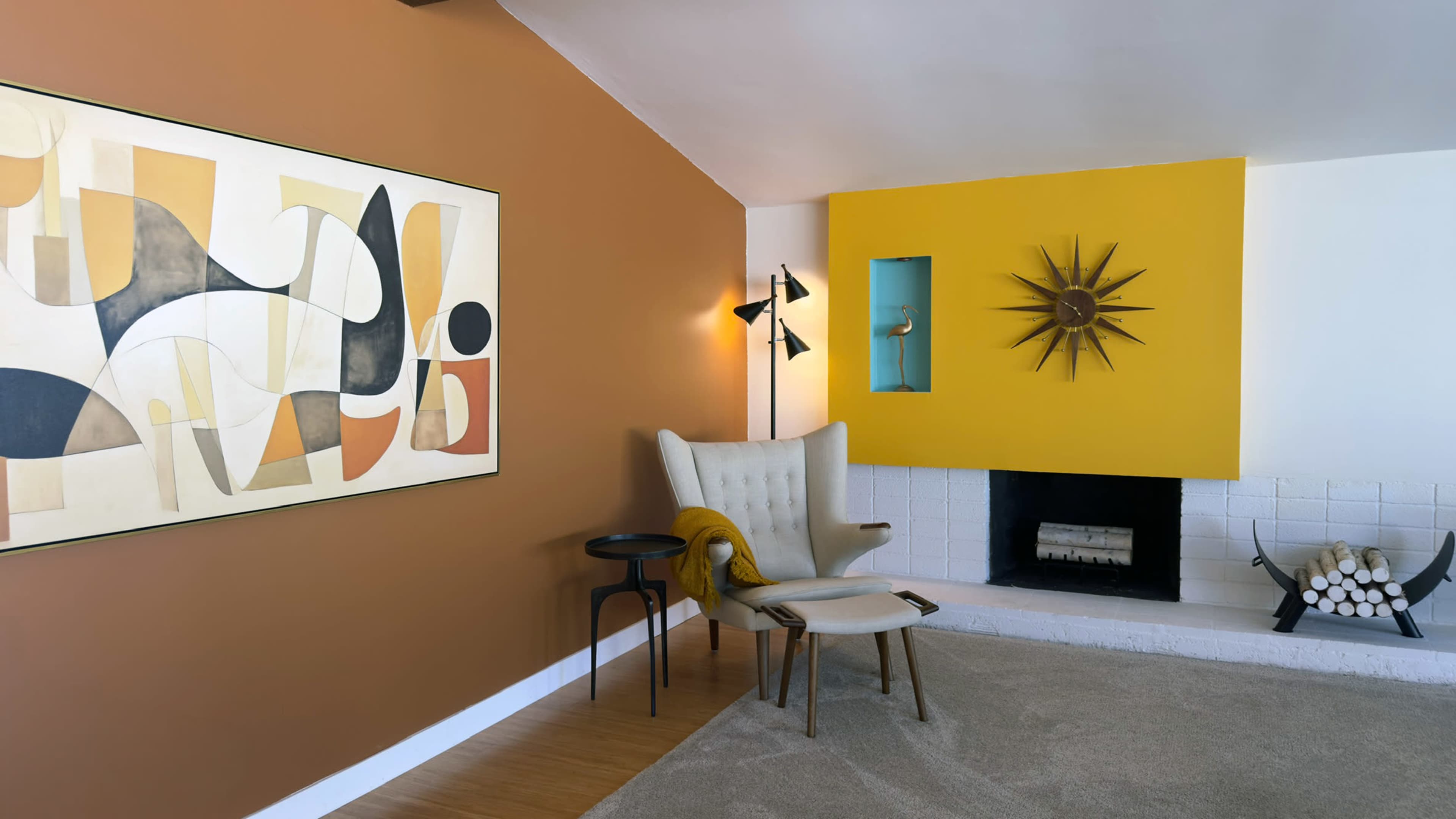 The image shows a modern living room with an orange and yellow accent wall, featuring a fireplace, a large abstract painting, and contemporary furniture.