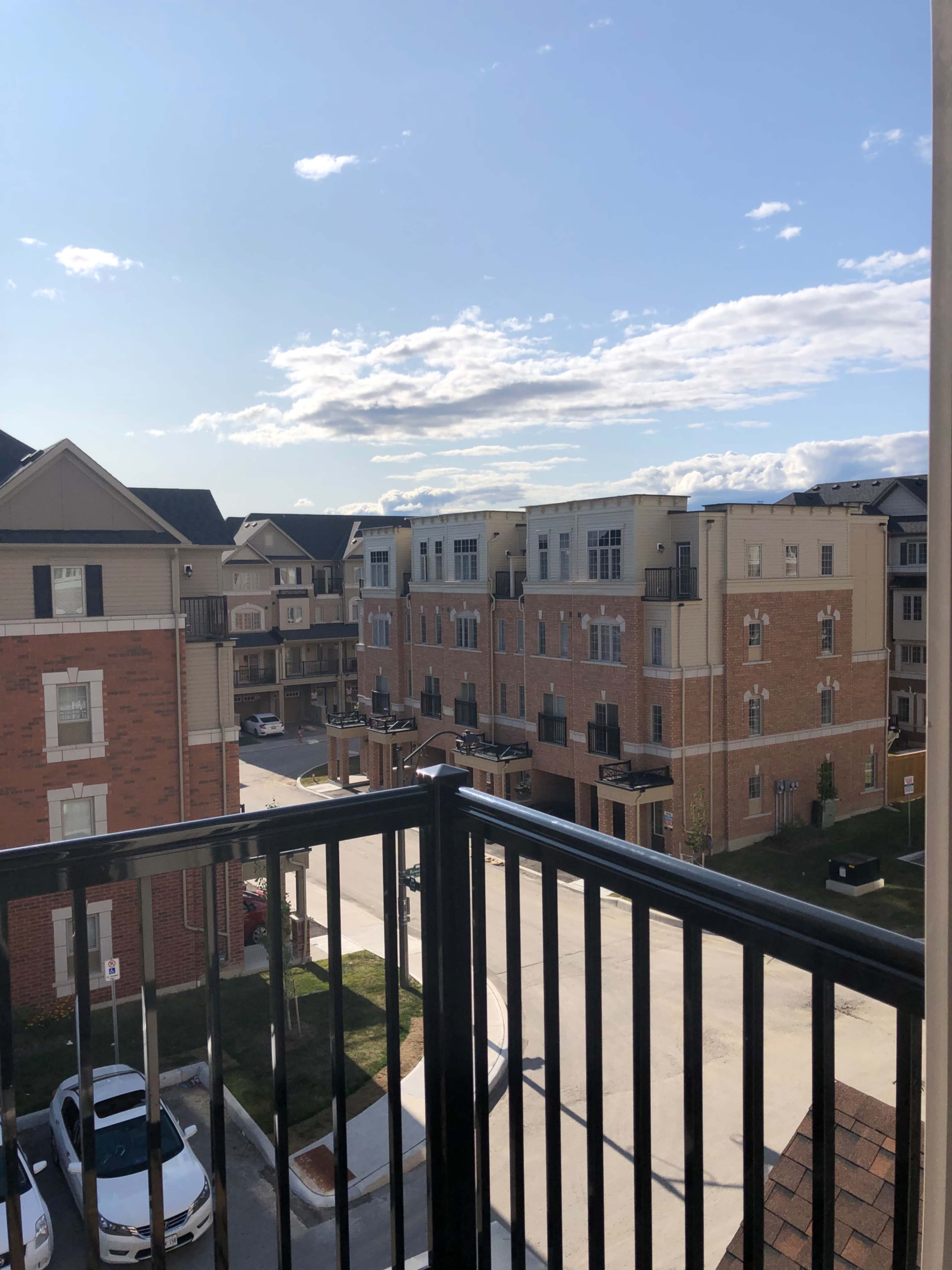 The image shows a view from a balcony overlooking a neighborhood with multiple townhouses and a clear sky.