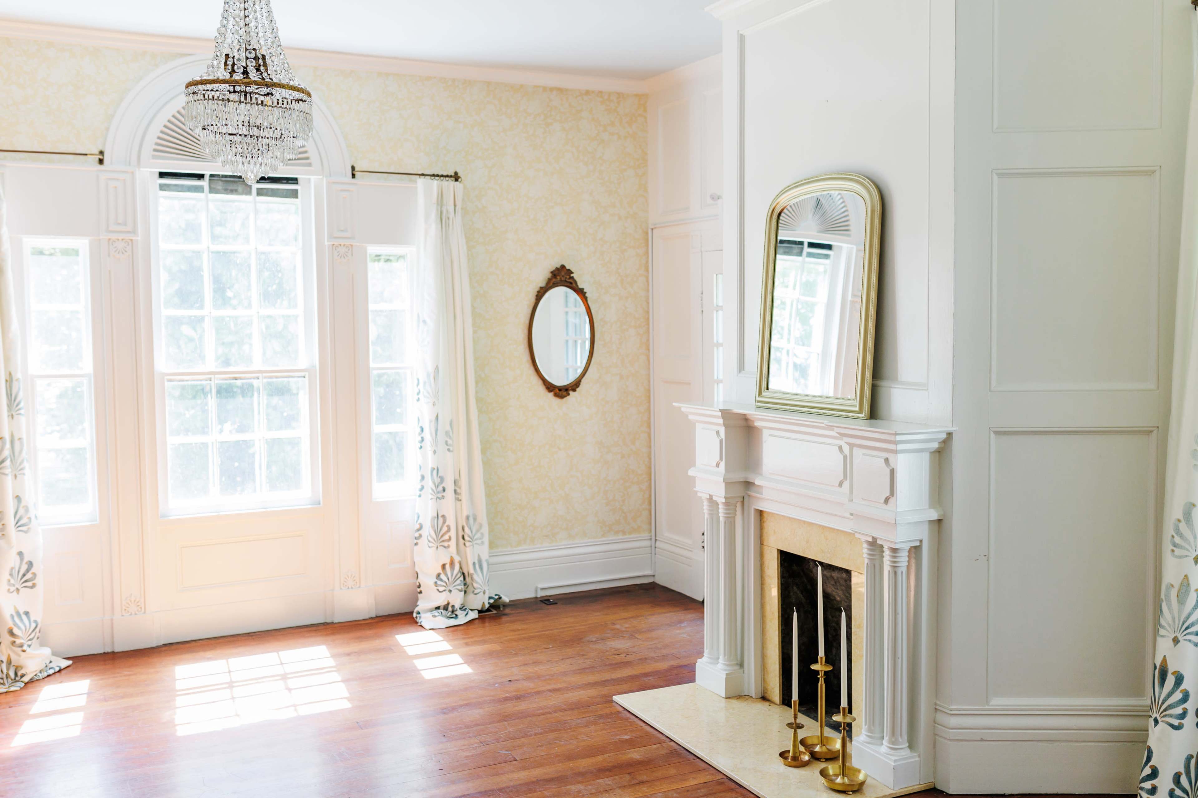 The room features large windows with natural light, hardwood floors, and a fireplace with two candlesticks beside it.