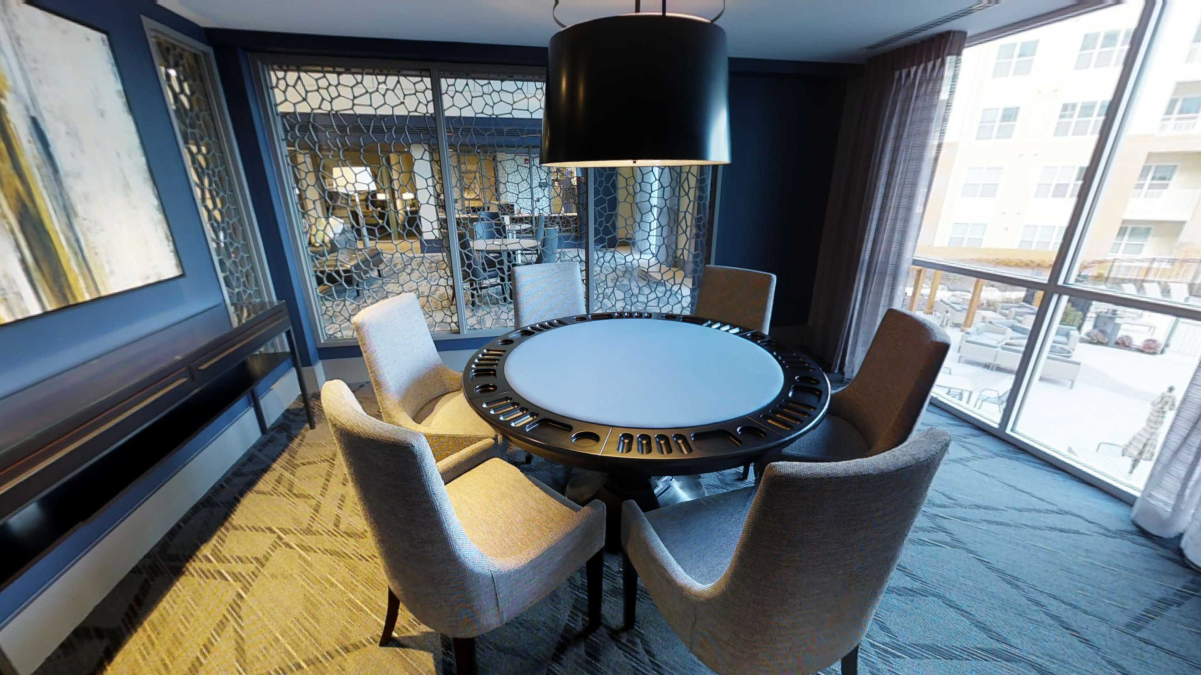 A modern conference room with a circular table surrounded by six chairs, featuring large windows that overlook an outdoor area.