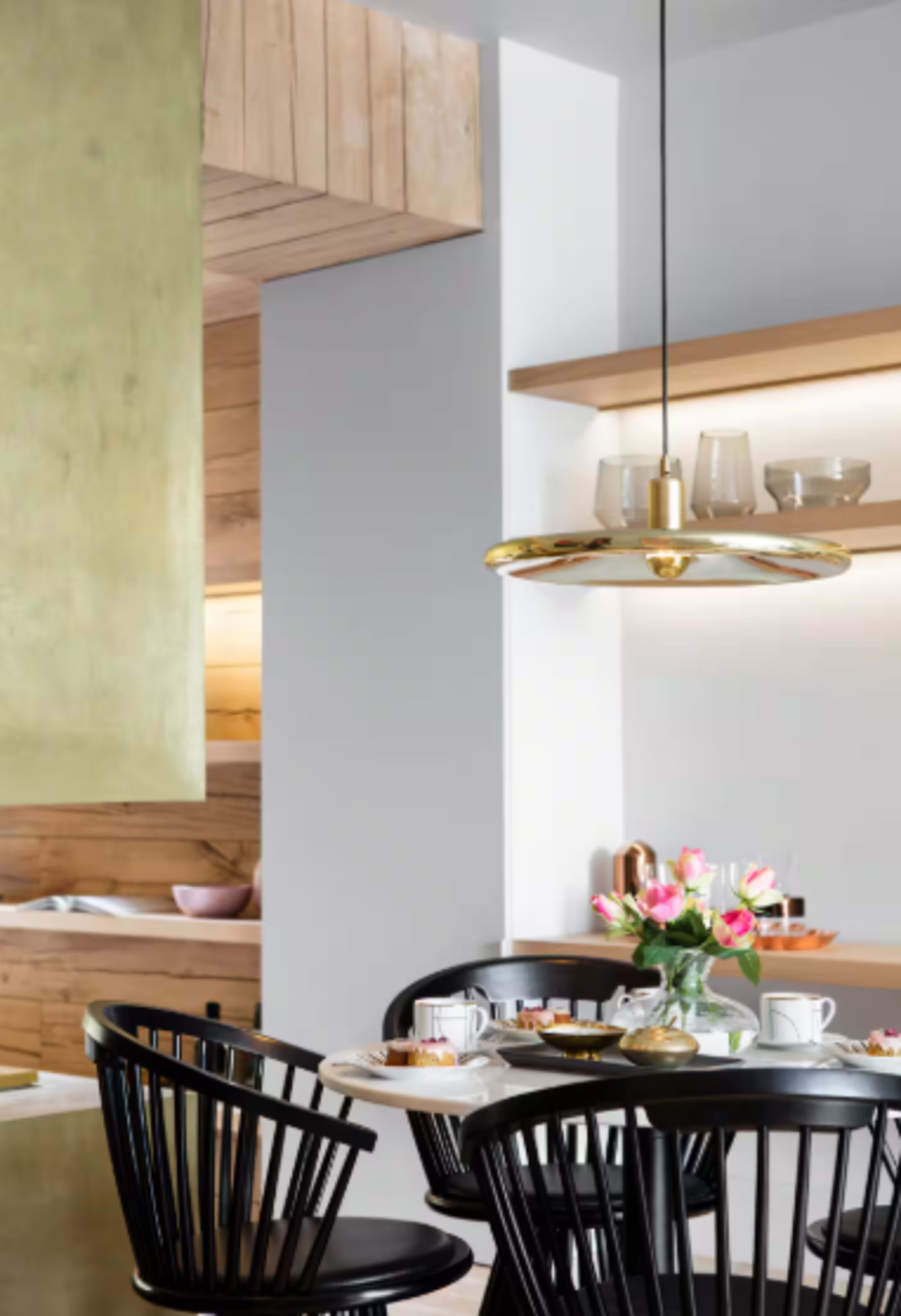 The image features a modern kitchen with a dining area, showcasing a round table with black chairs, a vase of flowers, and a pendant light above.