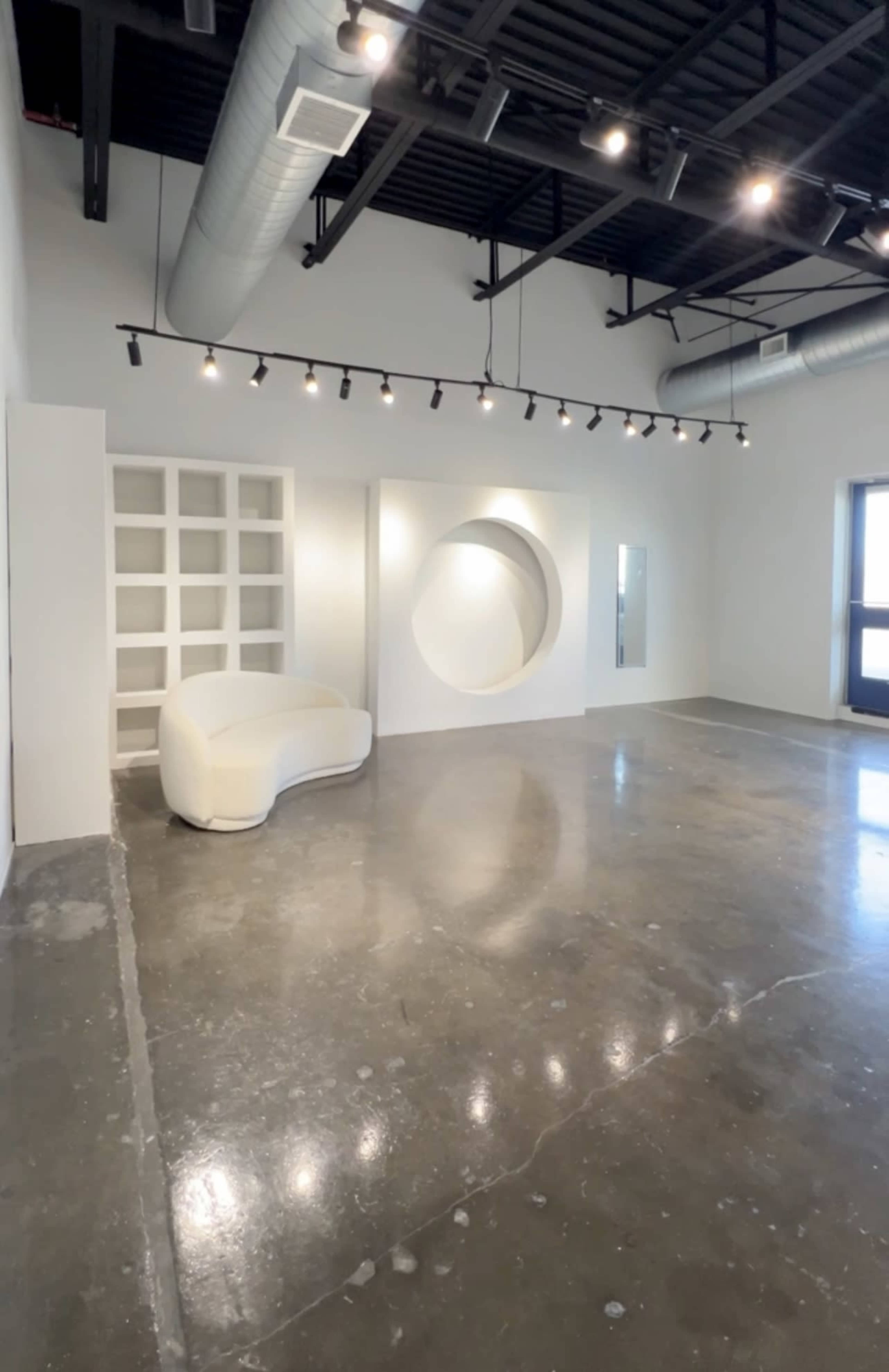 A spacious, minimalistic room with a white curved sofa, a circular wall feature, and large windows.
